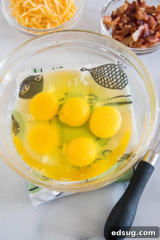 These bacon cheese egg muffins are packed with smoky crumbled bacon and melty cheddar. Enjoy these for brunch, or an easy on-the-go breakfast! Five eggs cracked into a glass bowl.