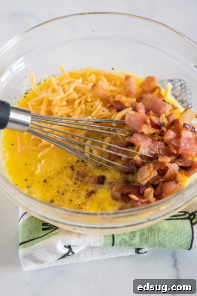 These bacon cheese egg muffins are packed with smoky crumbled bacon and melty cheddar. Enjoy these for brunch, or an easy on-the-go breakfast! Crumbled bacon and cheese added to a bowl of beaten eggs with a whisk.