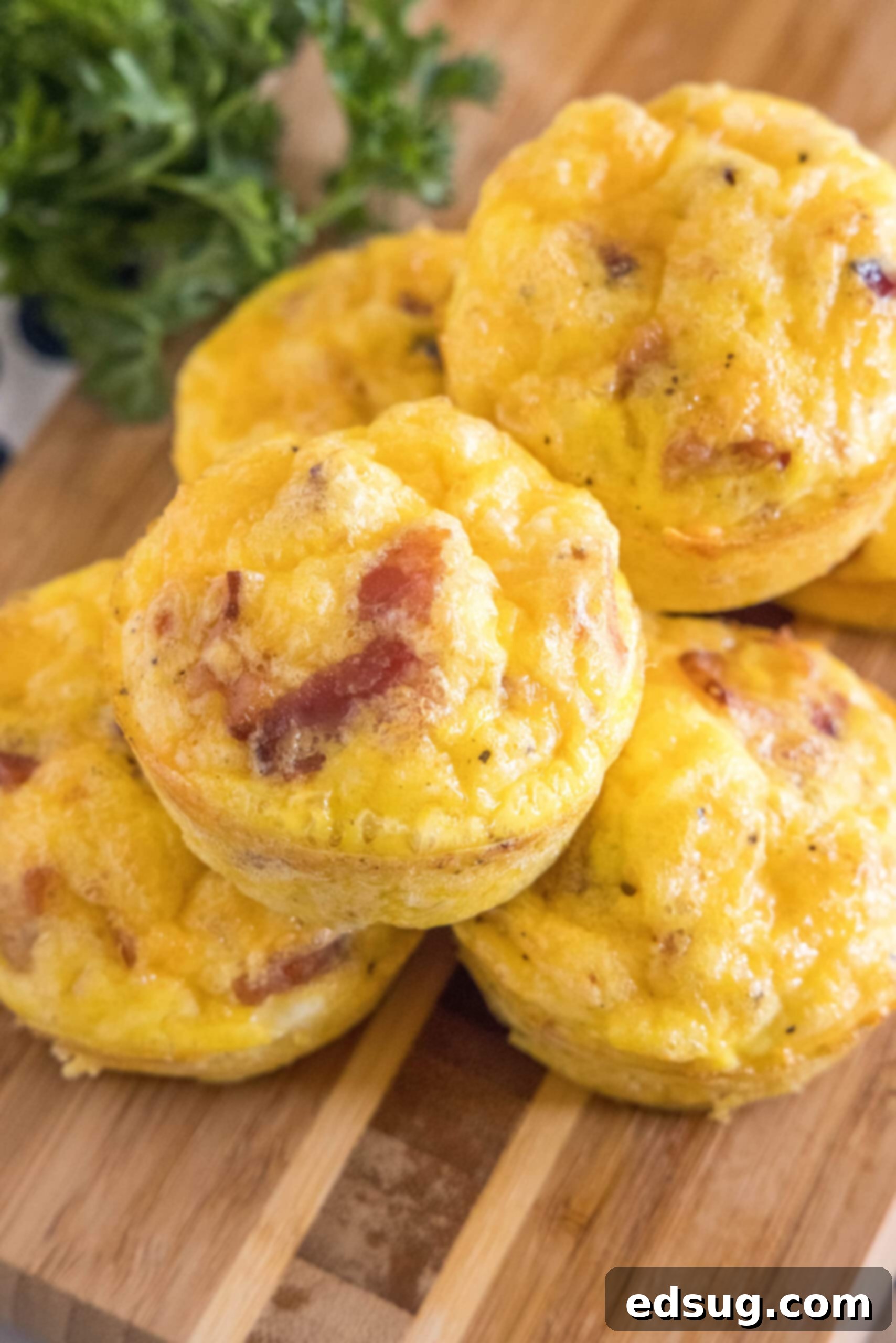 These bacon cheese egg muffins are packed with smoky crumbled bacon and melty cheddar. Enjoy these for brunch, or an easy on-the-go breakfast! Bacon cheese egg muffins stacked on a wooden cutting board.