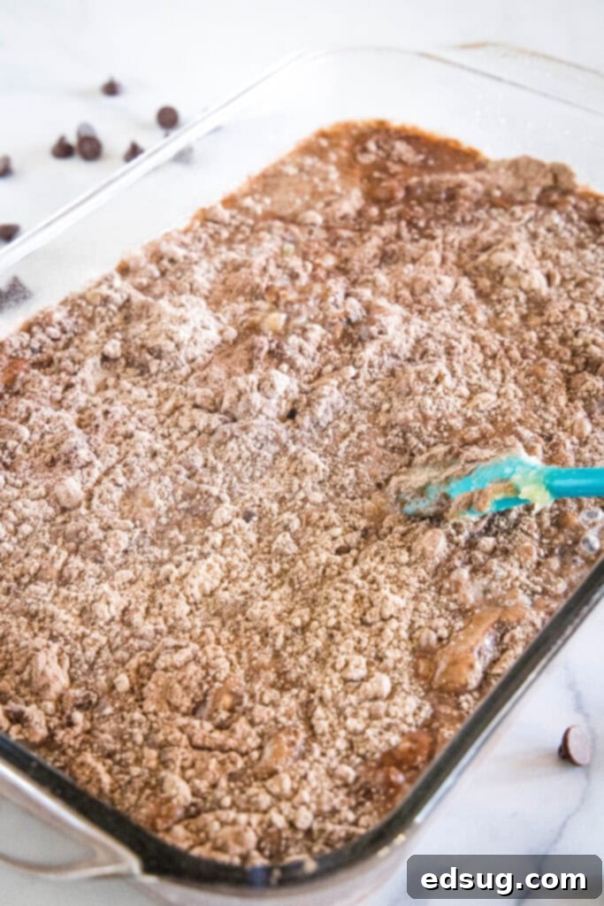 A spatula is used to barely stir the liquid ingredients into dry chocolate cake mix in a 9x13-inch glass baking dish.