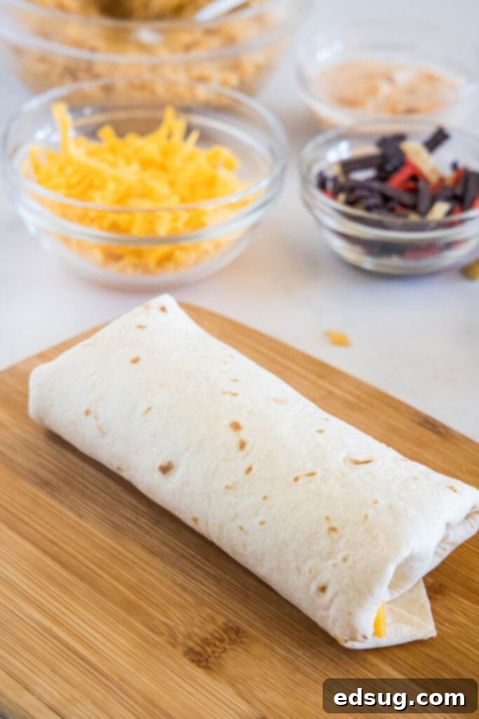 This copycat grilled cheese burrito recipe lets you remake an ooey-gooey Taco Bell favorite at home. Right down to the creamy chipotle sauce! A rolled burrito on a wooden cutting board with bowls of toppings in the background.