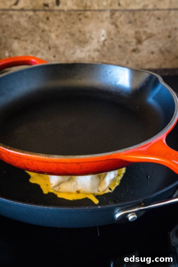 This copycat grilled cheese burrito recipe lets you remake an ooey-gooey Taco Bell favorite at home. Right down to the creamy chipotle sauce! A heavy-bottomed pan placed over top of a grilled cheese burrito in a skillet.