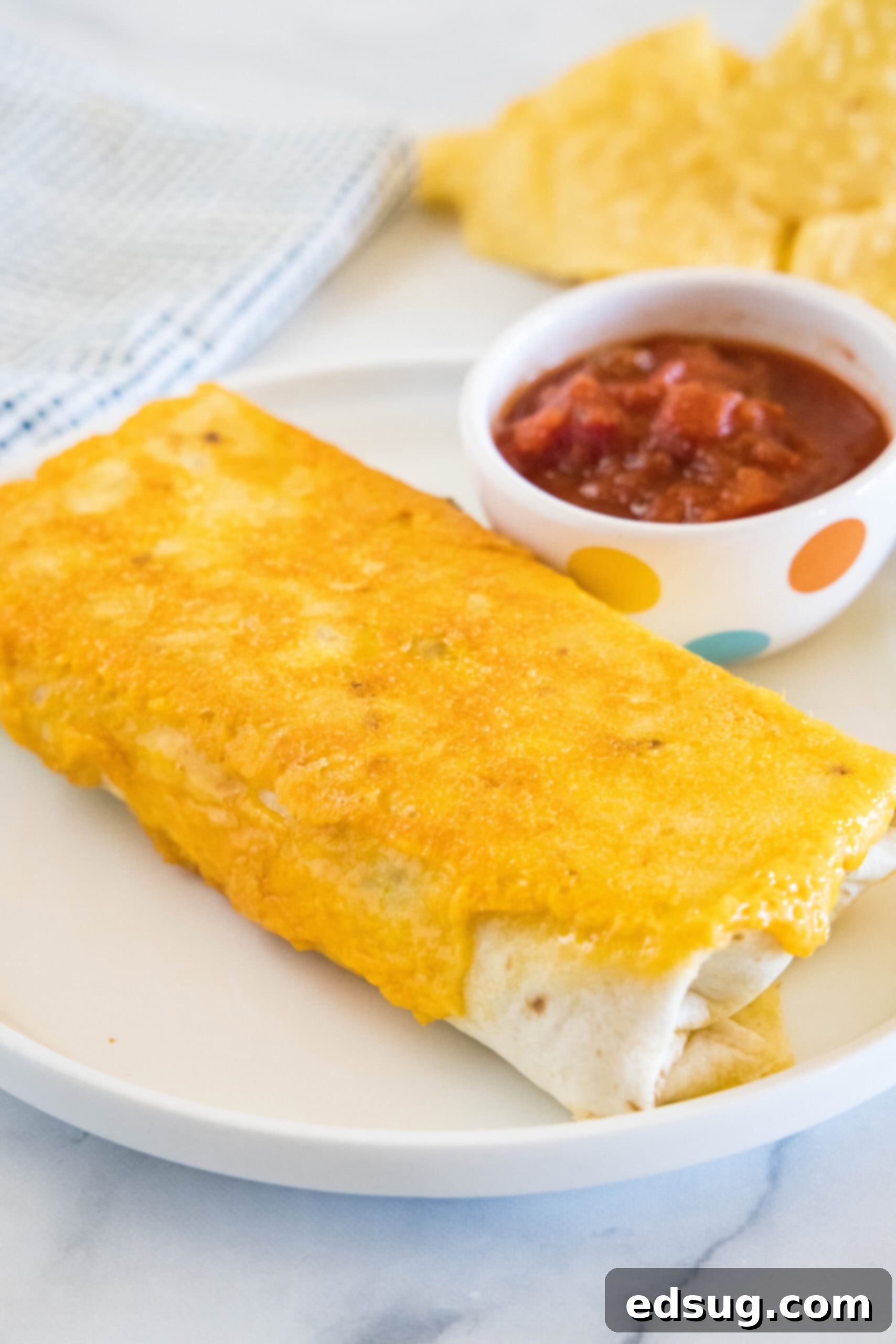 This copycat grilled cheese burrito recipe lets you remake an ooey-gooey Taco Bell favorite at home. Right down to the creamy chipotle sauce! A grilled cheese burrito next to salsa in a ramekin on a white plate.