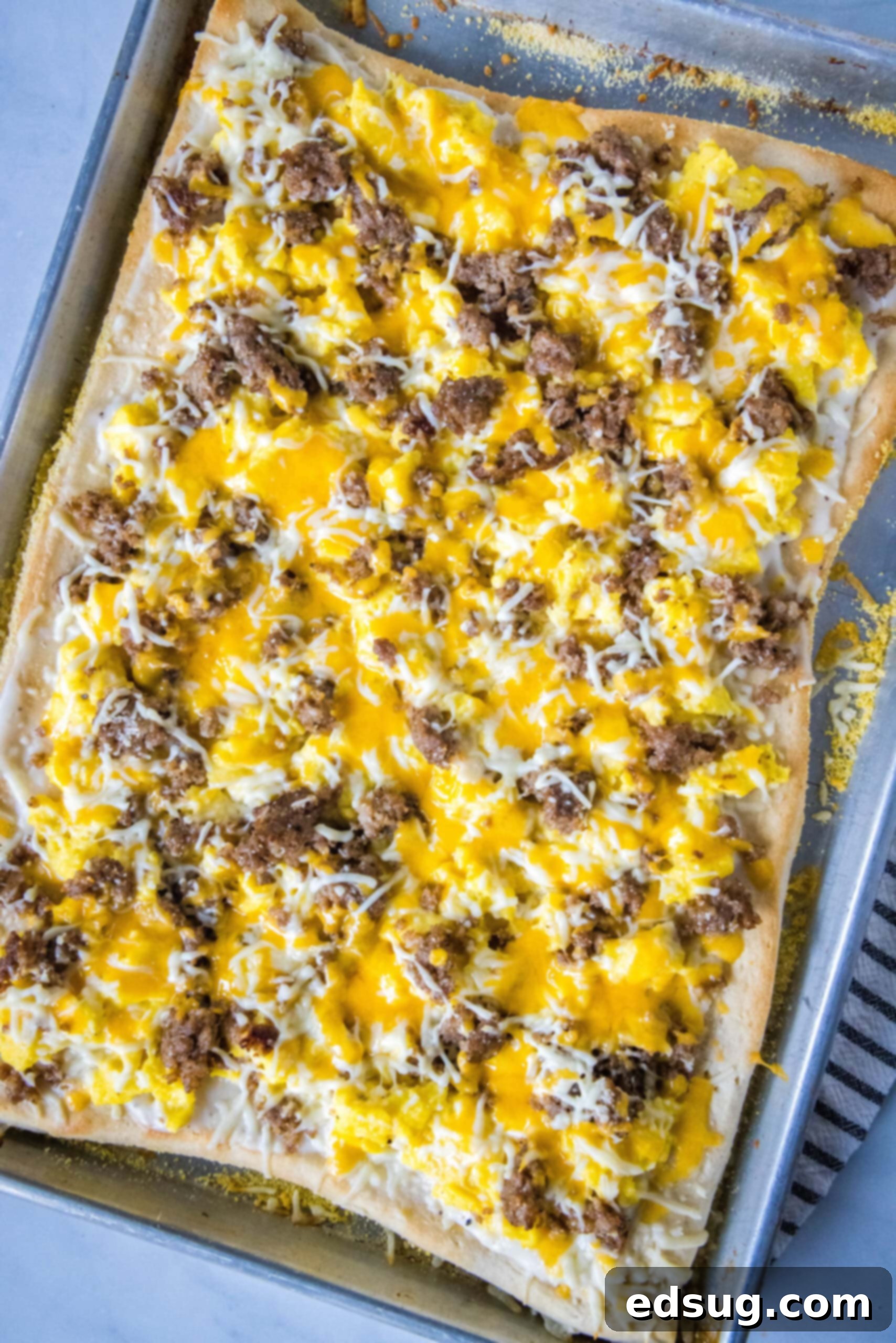 This satisfying breakfast pizza combines all of your breakfast favorites on top of a crispy pizza crust. It's so easy, baked in a sheet pan! Overhead view of a freshly baked breakfast pizza in a sheet pan, ready to be sliced.