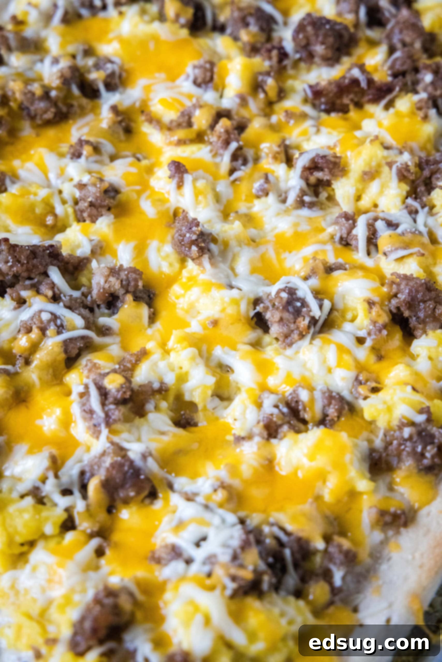 This satisfying breakfast pizza combines all of your breakfast favorites on top of a crispy pizza crust. It's so easy, baked in a sheet pan! Close up of a baked breakfast pizza topped with sausage, egg, and cheese, showing melted cheese and crispy crust.
