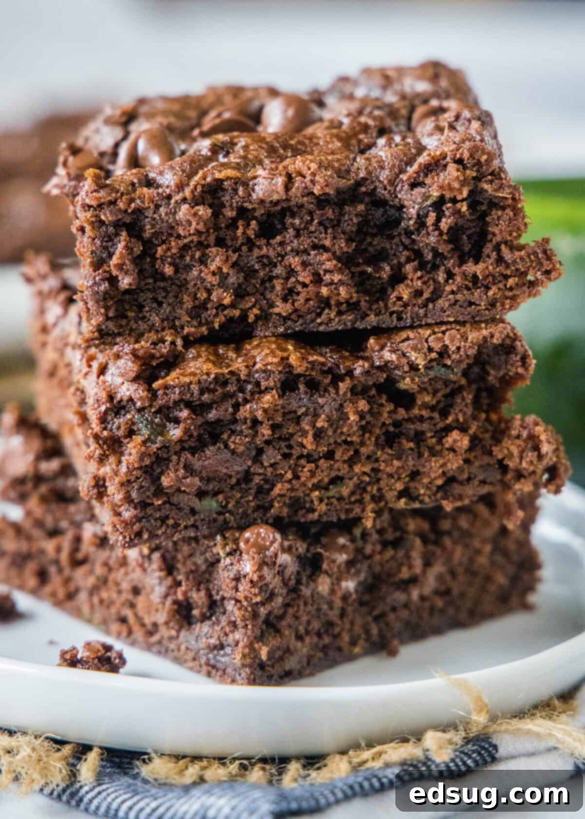 three fudgy zucchini brownies stacked on top of each other, showing their moist texture