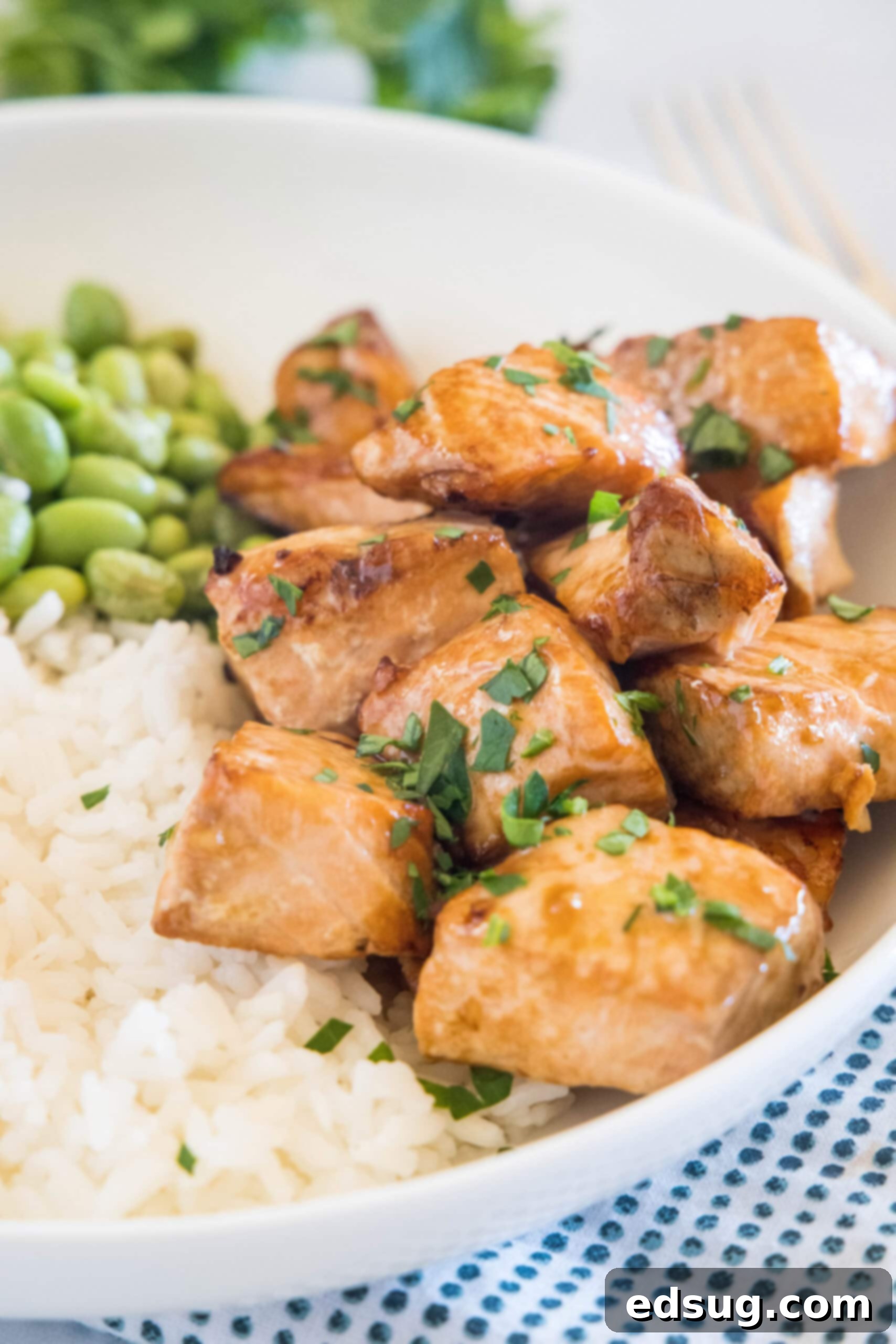 Tender and flaky salmon bites served with fluffy white rice and vibrant green edamame beans in a stylish white bowl, garnished with fresh herbs.