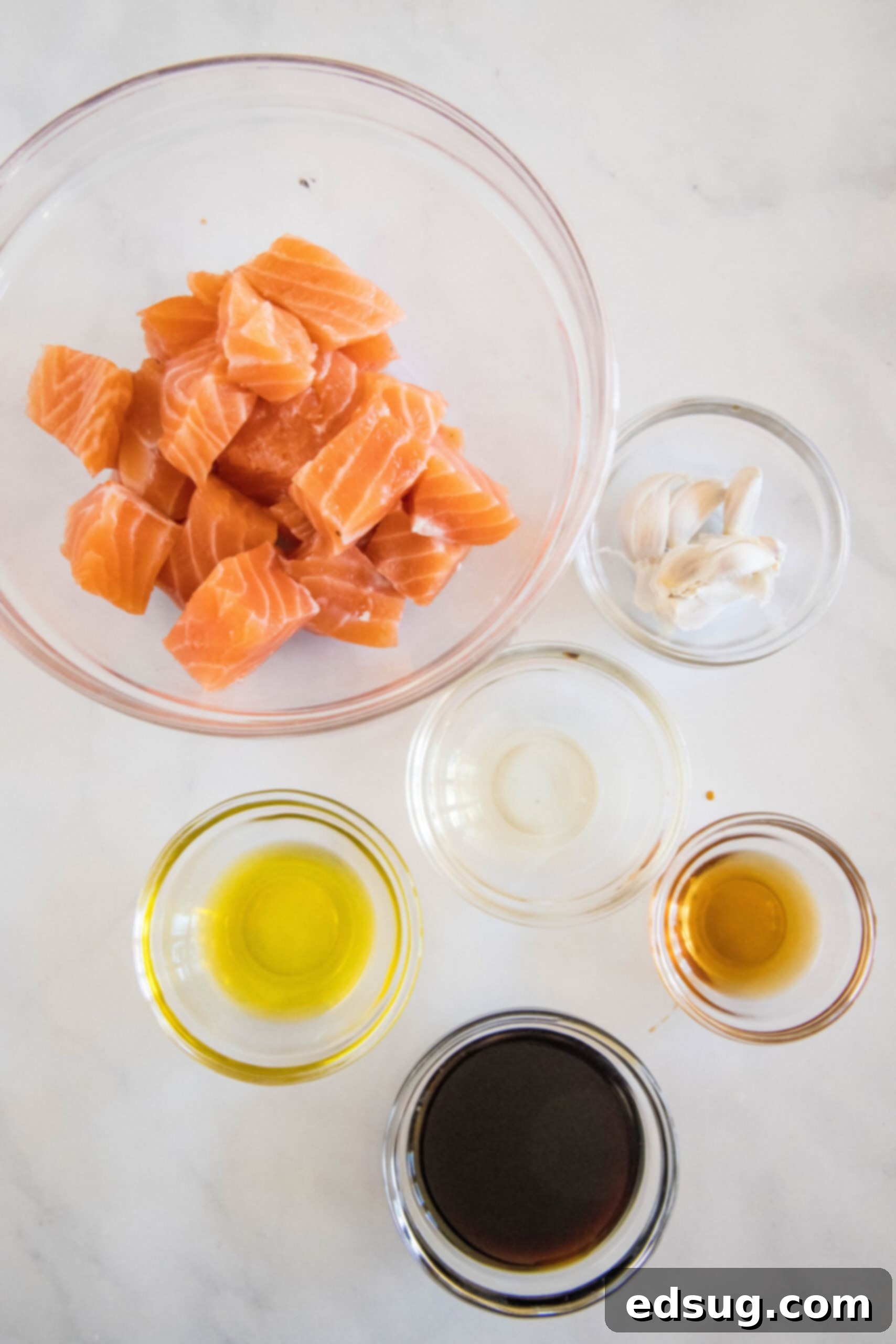 Fresh ingredients for making air fryer salmon bites, including salmon cubes, soy sauce, olive oil, rice vinegar, garlic, and sesame oil, laid out on a countertop.