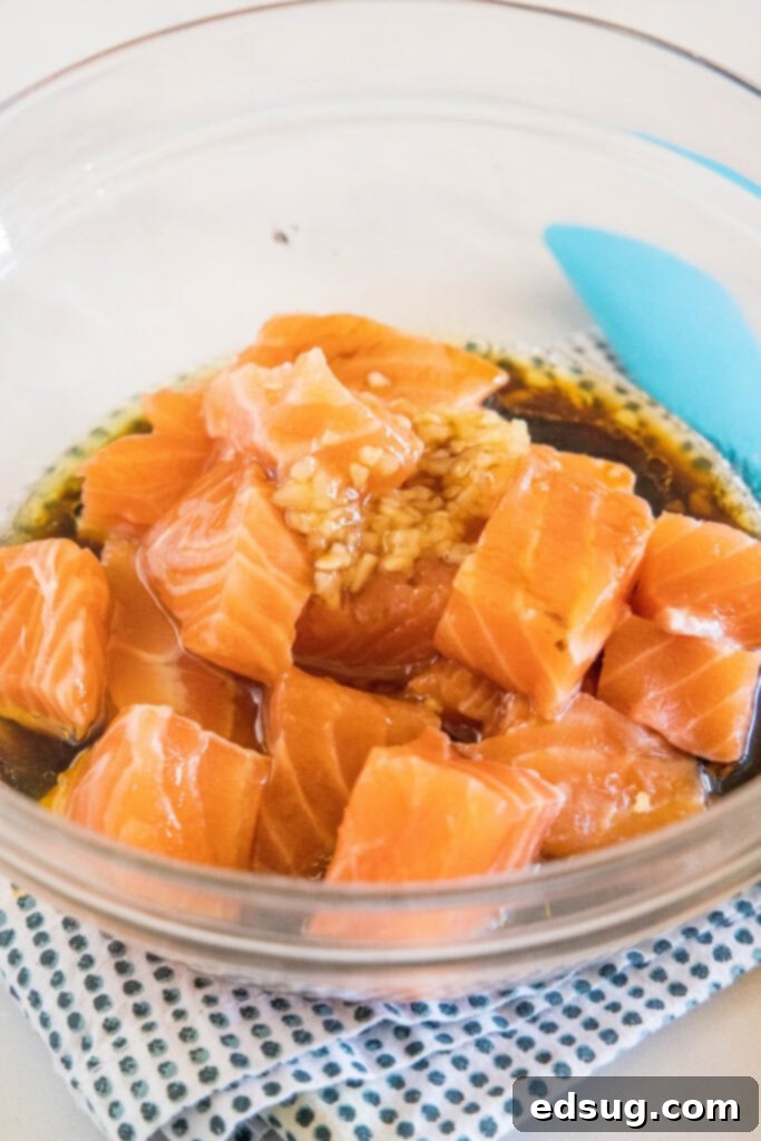 Bite-sized salmon pieces gently mixed with a rich soy-based marinade in a clear glass bowl, ready for flavor infusion.