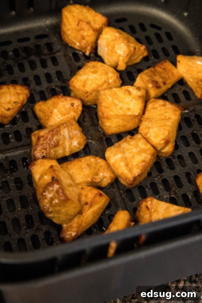 Perfectly cooked, golden-brown salmon bites resting inside the air fryer basket after cooking, showcasing their crispy exterior and juicy interior.