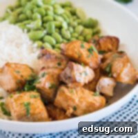 Salmon bites served with rice and edamame beans in a white bowl.