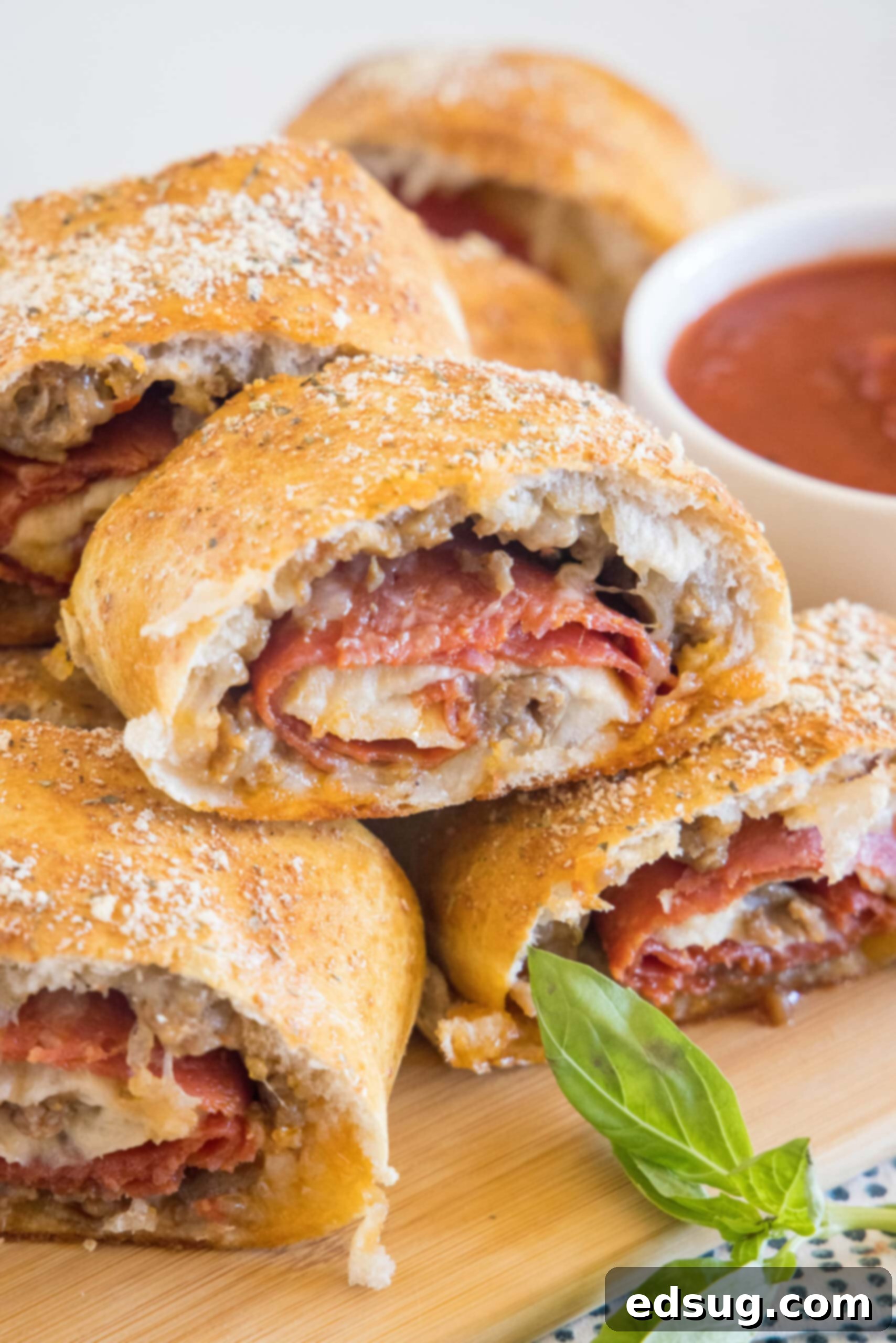 Put a fun spin on pizza night with this easy pizza bread recipe. Roll your favorite pizza toppings inside a pizza crust, bake, and slice! #pizzabread #pizza Pizza bread slices stacked on a wooden board next to a bowl of pizza sauce for dipping.