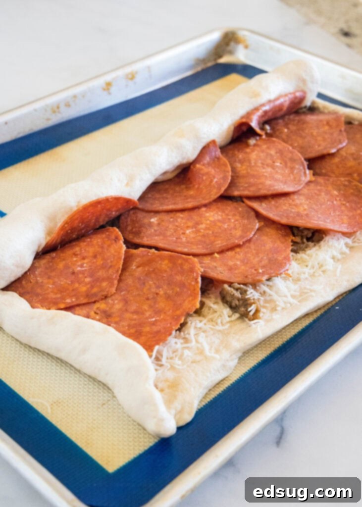Put a fun spin on pizza night with this easy pizza bread recipe. Roll your favorite pizza toppings inside a pizza crust, bake and slice! #pizzabread #pizza Pizza dough filled with toppings and partially rolled into a log on a baking sheet.