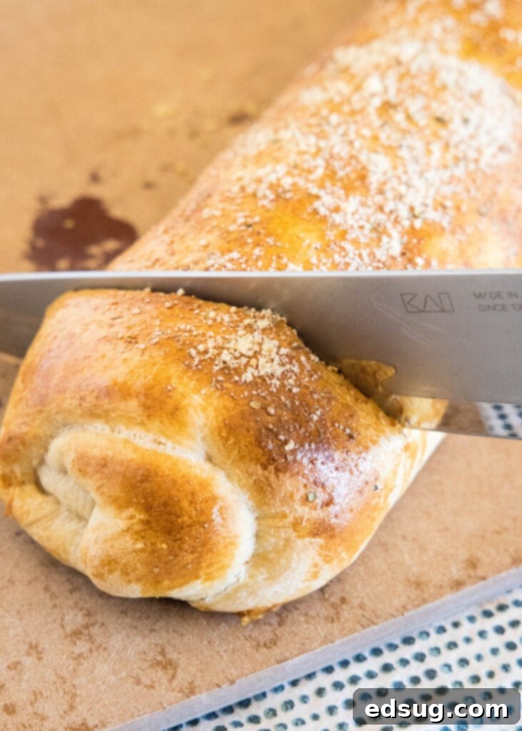 Put a fun spin on pizza night with this easy pizza bread recipe. Roll your favorite pizza toppings inside a pizza crust, bake, and slice! #pizzabread #pizza A knife slicing into the end of a baked pizza bread roll.