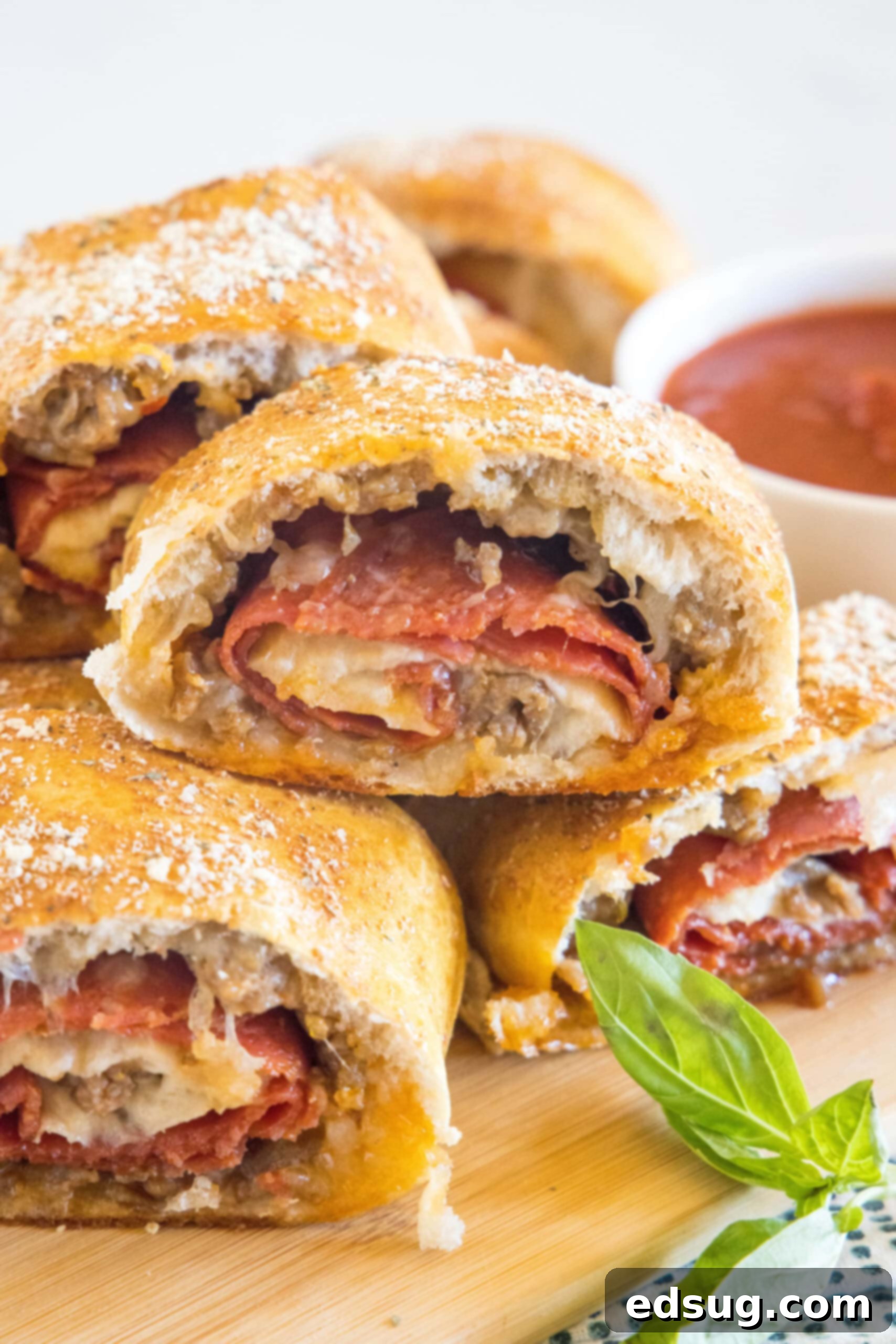 Put a fun spin on pizza night with this easy pizza bread recipe. Roll your favorite pizza toppings inside a pizza crust, bake, and slice! #pizzabread #pizza Pizza bread slices stacked on a wooden board next to a bowl of pizza sauce for dipping.