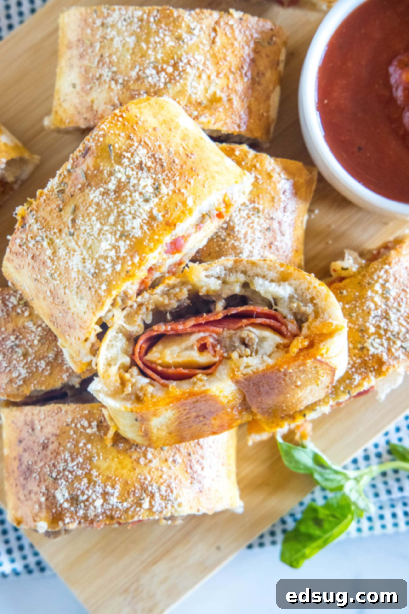 Put a fun spin on pizza night with this easy pizza bread recipe. Roll your favorite pizza toppings inside a pizza crust, bake and slice! #pizzabread #pizza Overhead view of pizza bread slices stacked on a wooden board next to a bowl of pizza sauce for dipping.