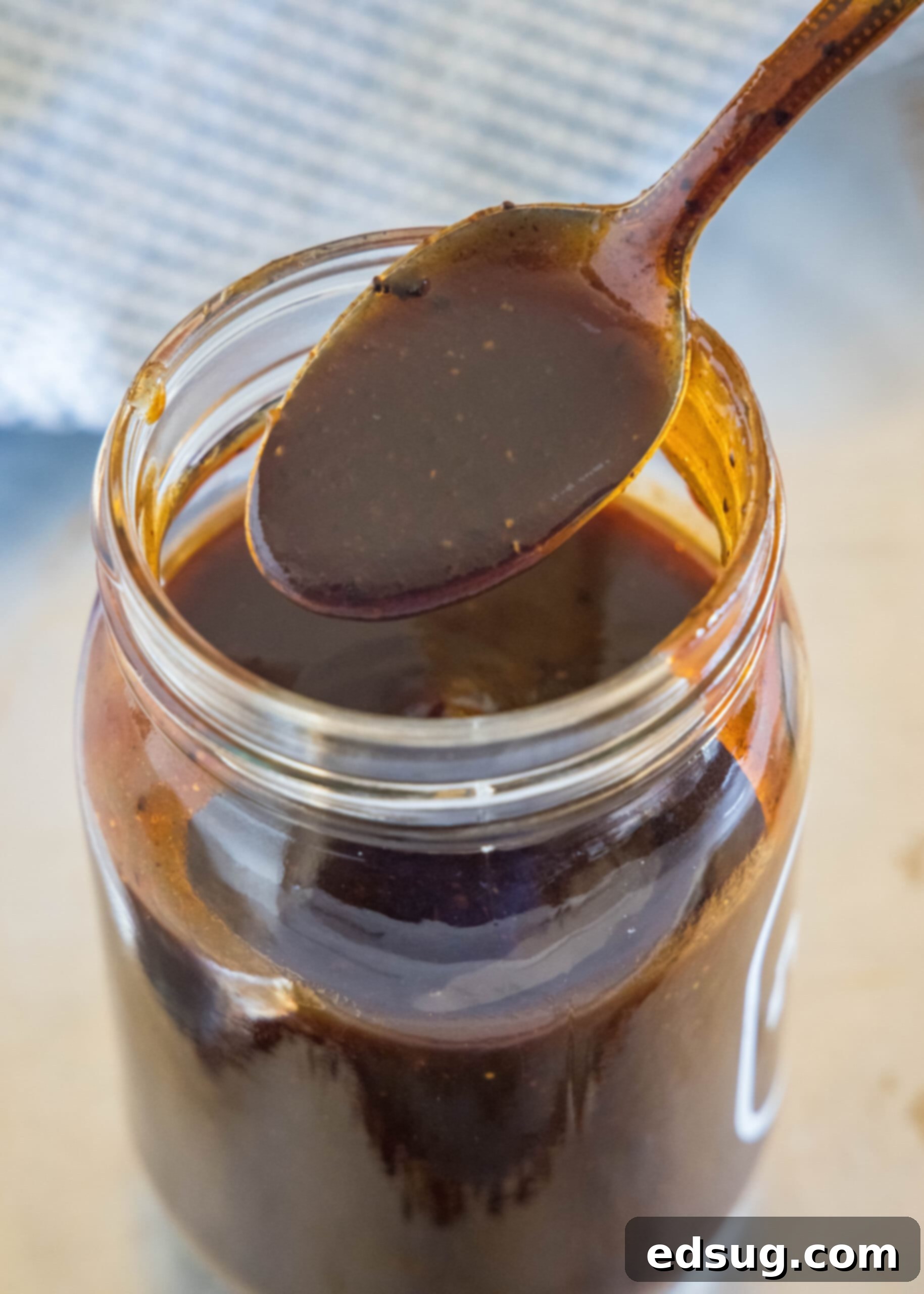 This easy homemade barbecue sauce tastes way better than store-bought! It’s sweet, tangy, and perfect on wings, ribs, grilled meat, and more. A spoonful of homemade barbecue sauce held over a mason jar.