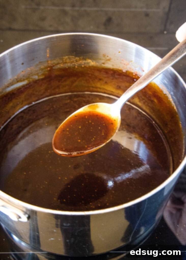 This easy homemade barbecue sauce tastes way better than store-bought! It’s sweet, tangy, and perfect on wings, ribs, grilled meat, and more. A spoonful of homemade barbecue sauce held over a pot of sauce on the stovetop.