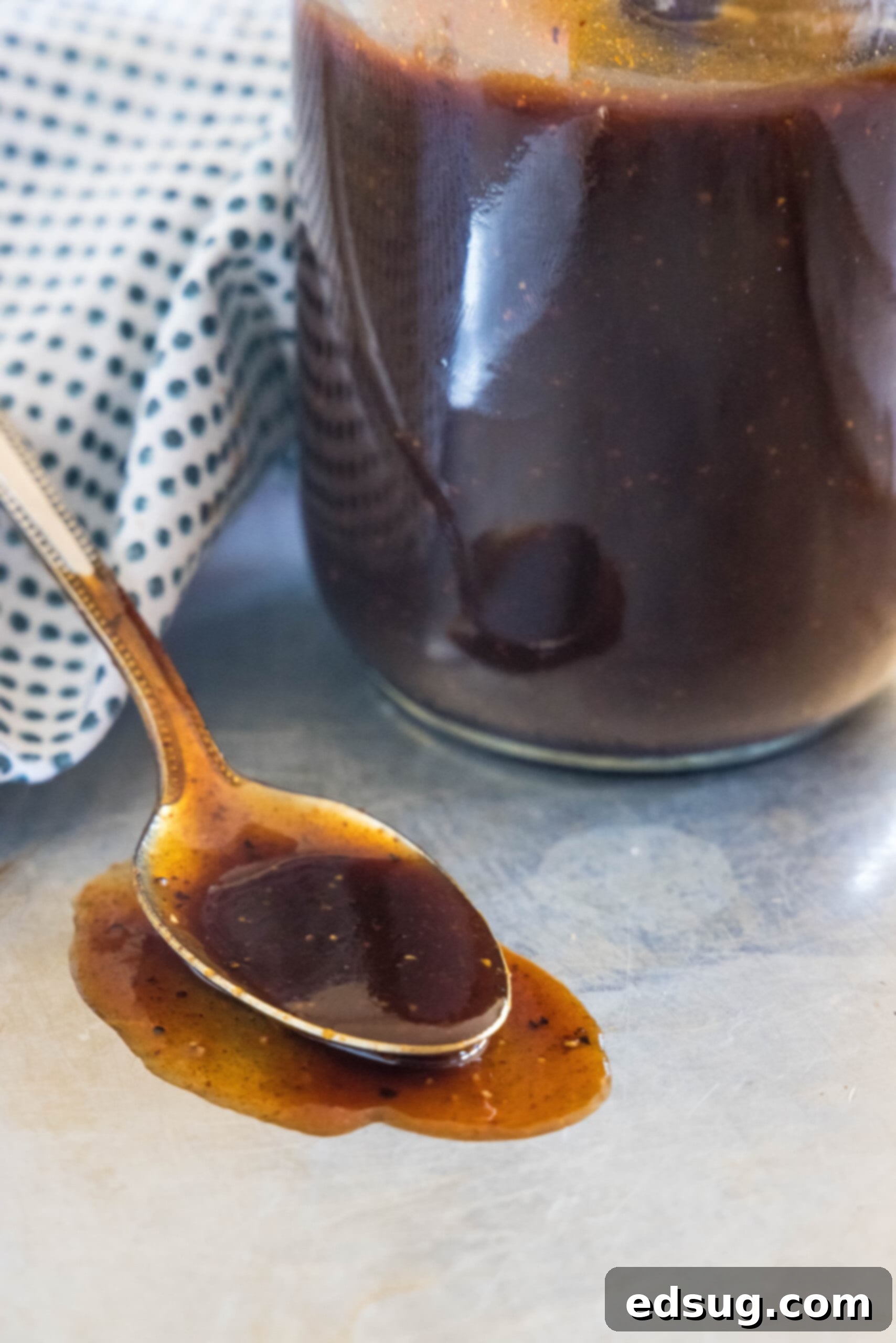 This easy homemade barbecue sauce tastes way better than store-bought! It’s sweet, tangy, and perfect on wings, ribs, grilled meat, and more. A spoonful of homemade barbecue sauce laying on a tabletop next to more sauce in a mason jar.