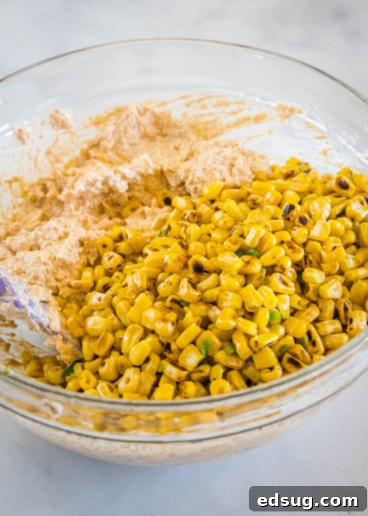 Corn kernels added to dip ingredients in a glass bowl.