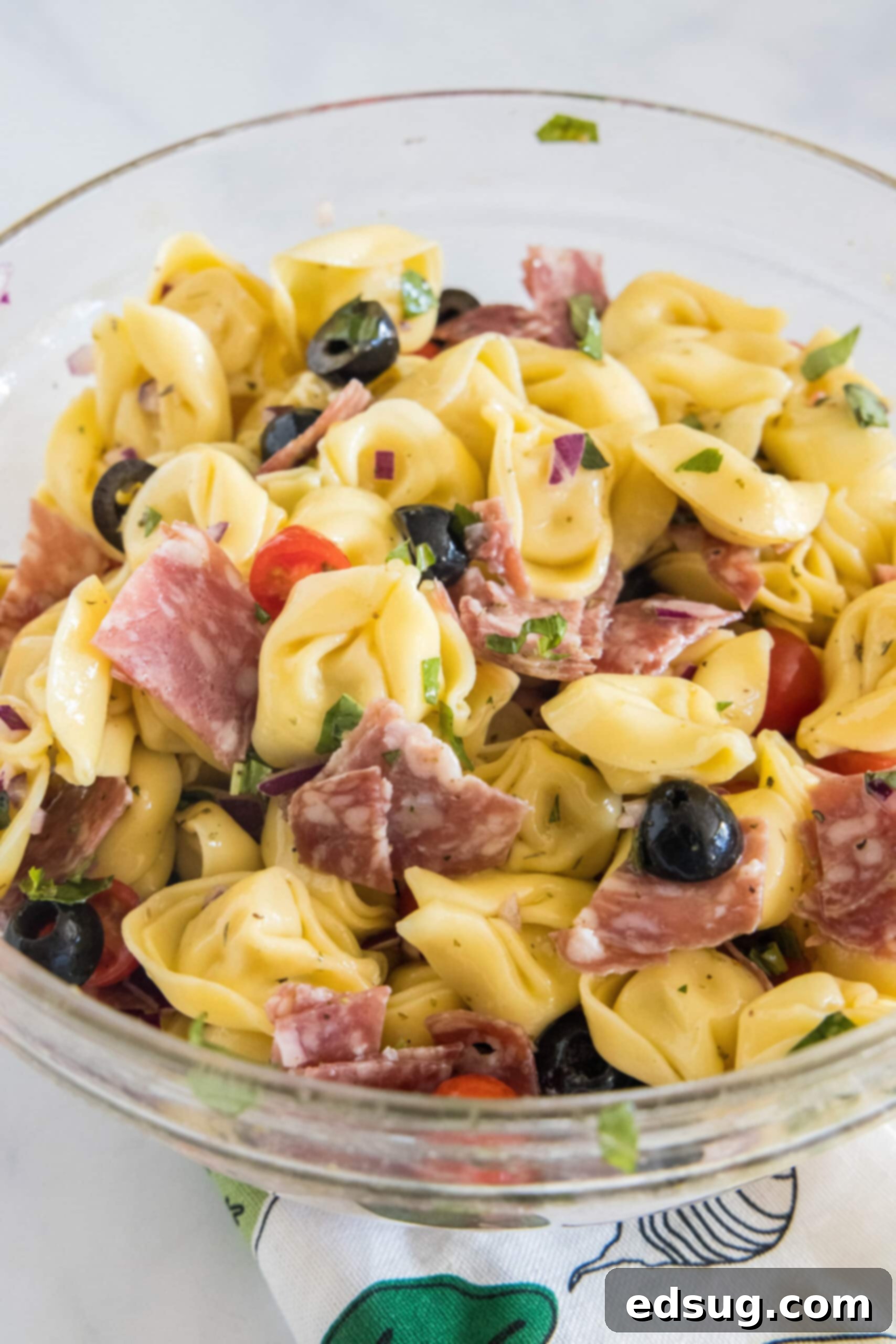 A close-up view of the prepared tortellini pasta salad resting in a transparent glass bowl, with all ingredients visibly mixed and coated.