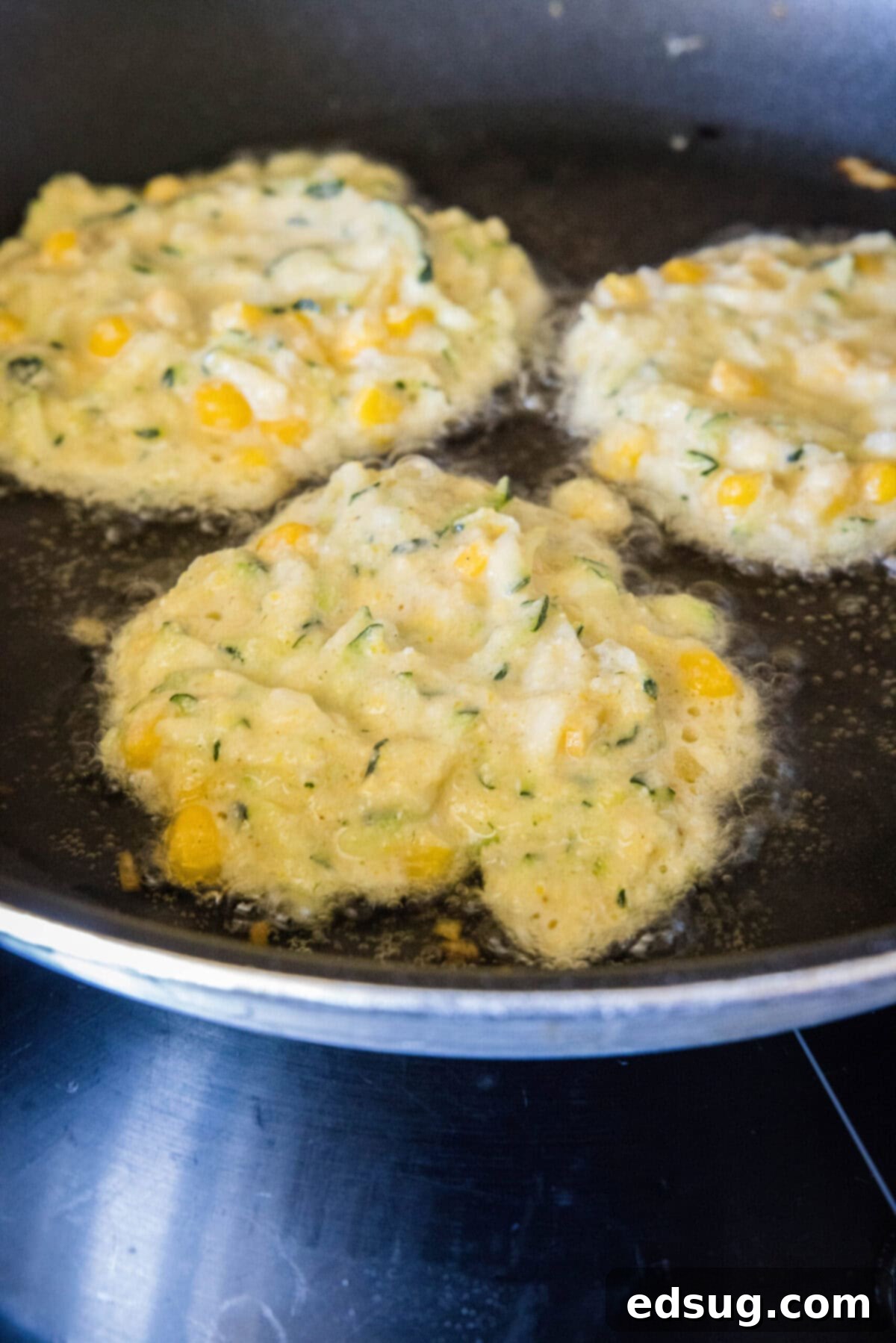 These easy zucchini fritters with corn are light, crispy, moist, and only take 25 minutes to make. They're a perfect side dish or snack! Three raw zucchini and corn fritters sizzling in a hot skillet, beginning to crisp and brown.