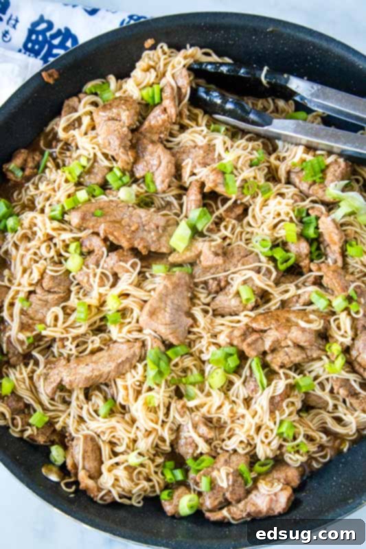 Pork lo mein in large skillet with tongs, ready to serve