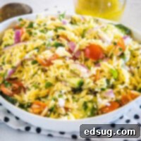 Orzo pasta salad in a large bowl resting on top of a black and white polka dot dishcloth, with a jar of dressing in the background.