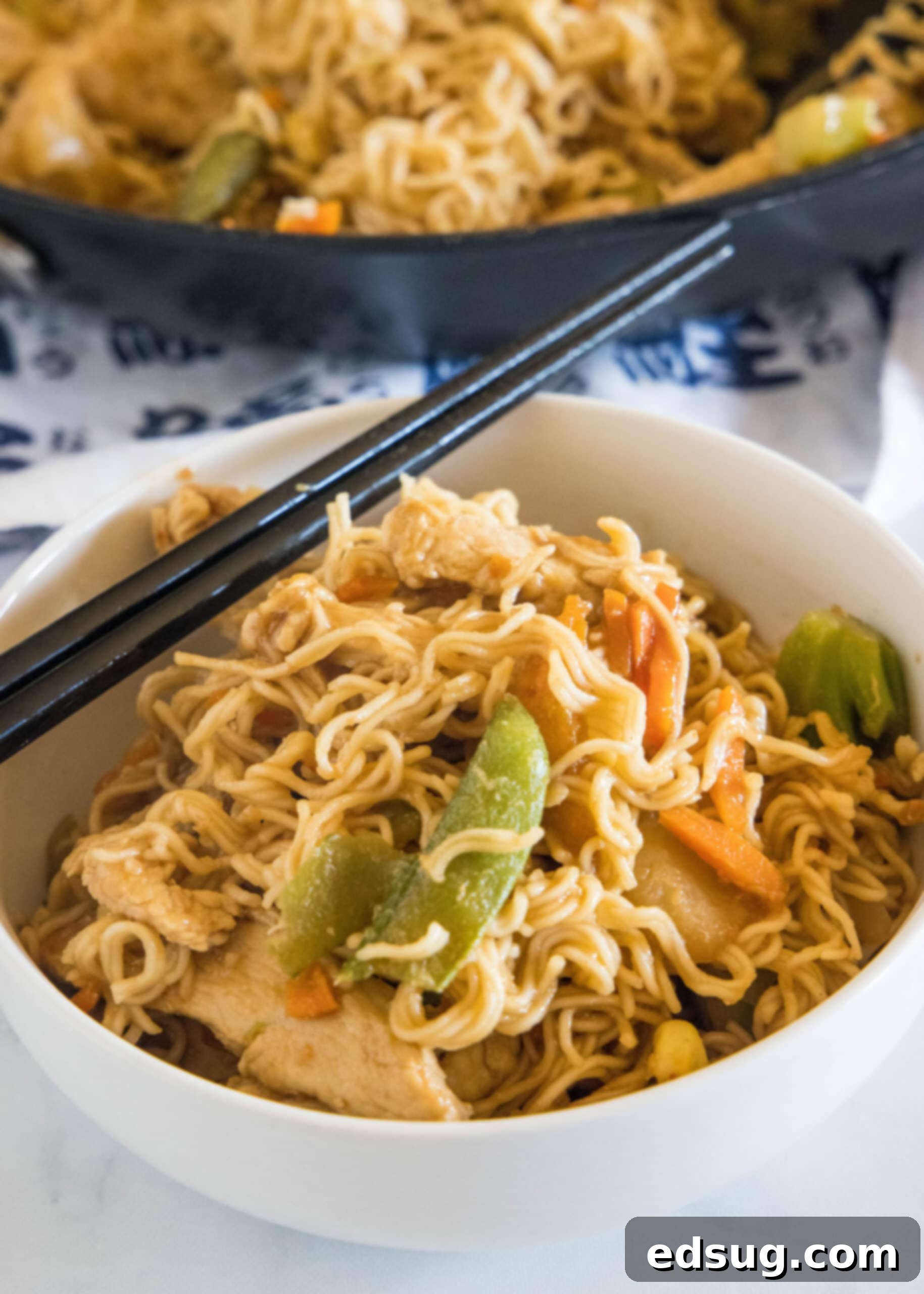 This 20-minute ramen stir fry is an easy meal packed with juicy chicken, veggies, and silky ramen noodles in a flavor-loaded stir fry sauce. Ramen stir fry in a white bowl with a set of chopsticks resting on the rim of the bowl, garnished with sesame seeds and green onions.
