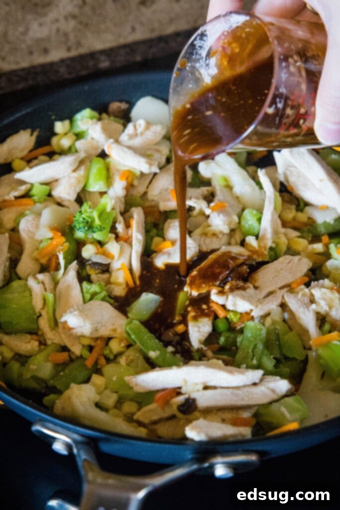 Stir fry sauce is poured over chicken and vegetables in a skillet. Stir fry sauce is poured over chicken and vegetables in a skillet.