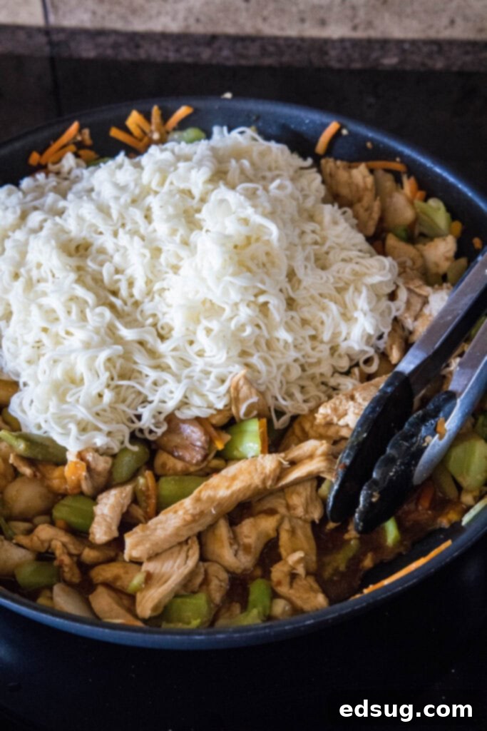 Cooked ramen noodles added to a skillet with chicken, veggies, and stir fry sauce. Cooked ramen noodles added to a skillet with chicken, veggies, and stir fry sauce.