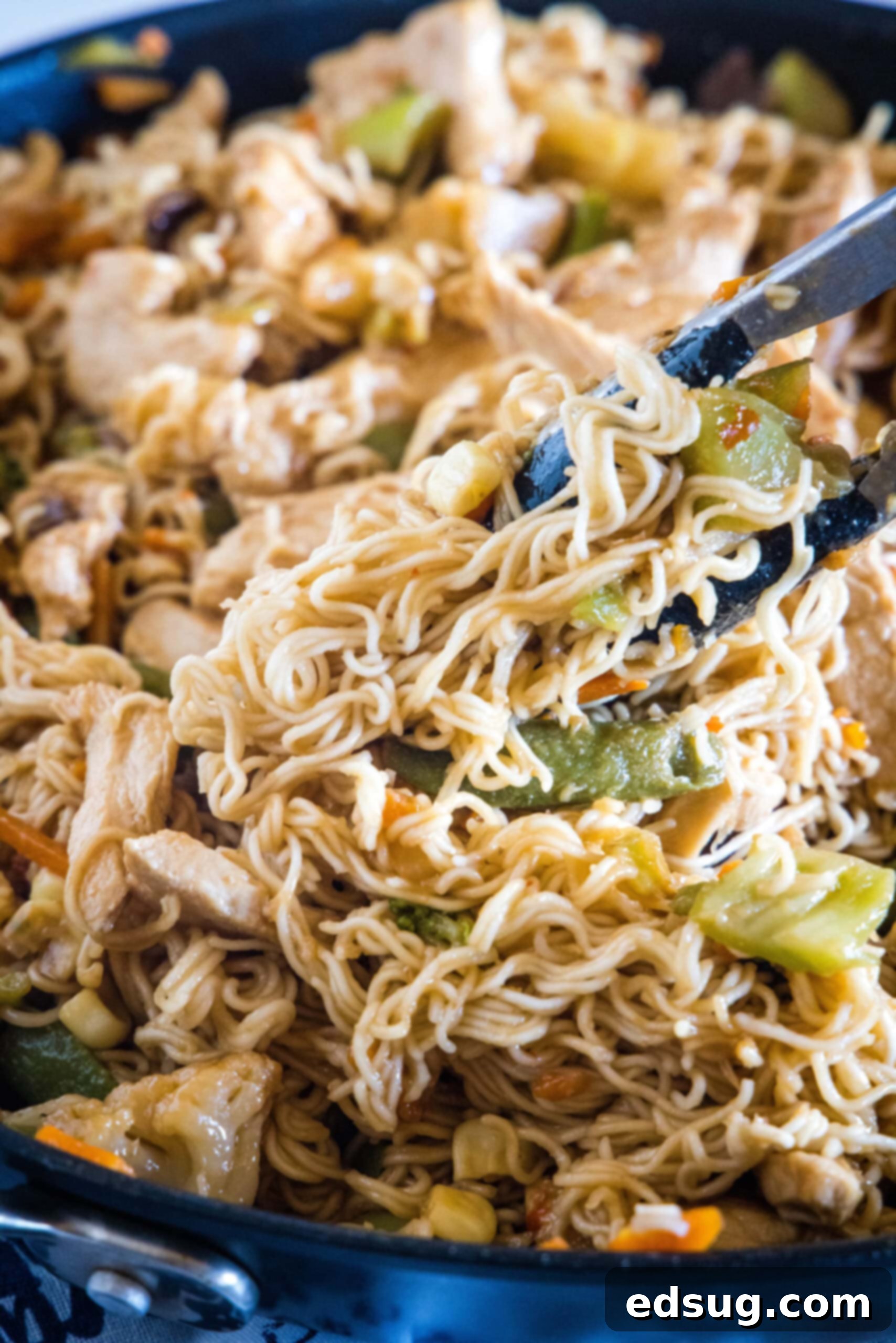 Tongs lifting a serving of ramen stir fry from a skillet. Tongs lifting a serving of ramen stir fry from a skillet into a bowl.