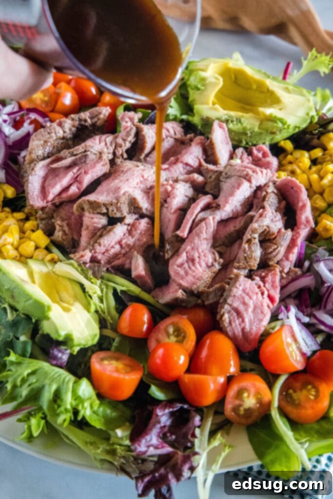 Dressing is drizzled over a large platter of steak salad.