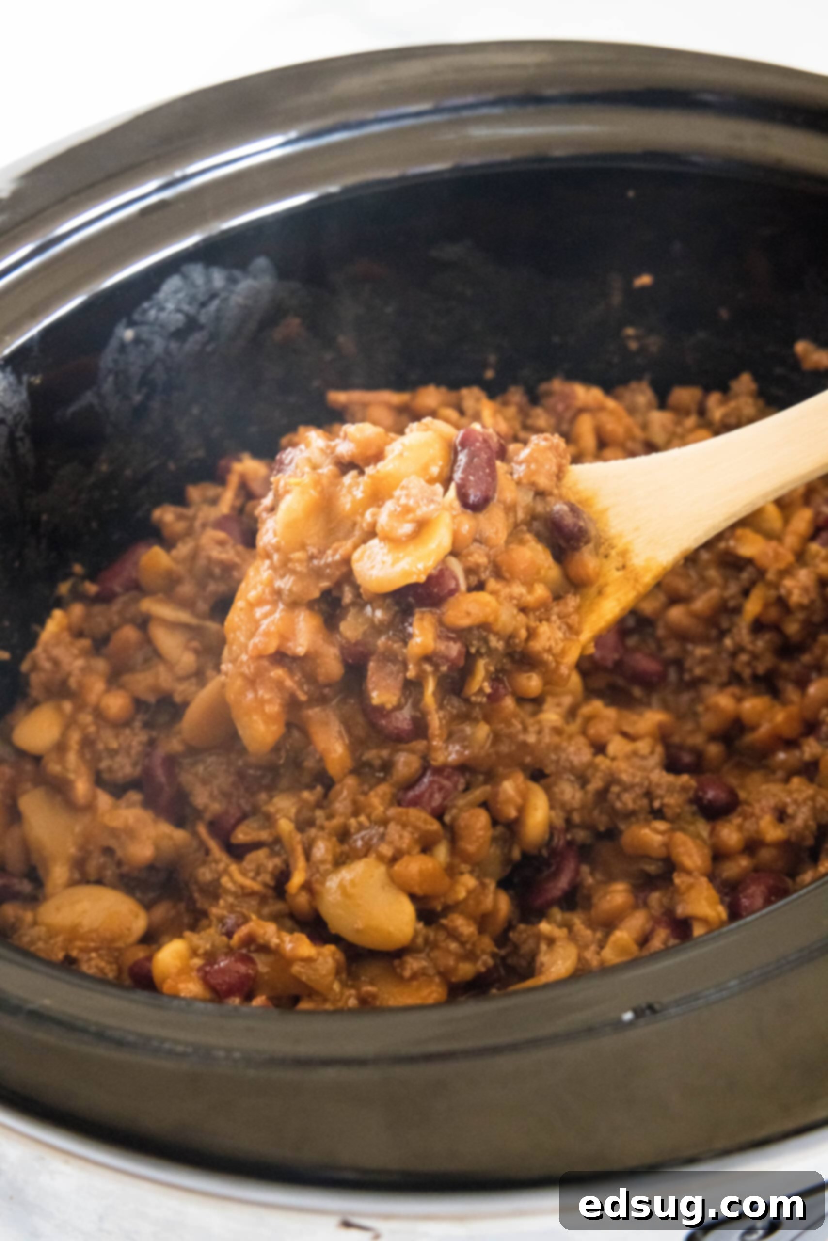 This hearty calico beans recipe is a sweet n' smoky side dish perfect for cookouts, potlucks, and holidays. Make it in the oven or crock pot! A spoon lifting calico beans from a crock pot.