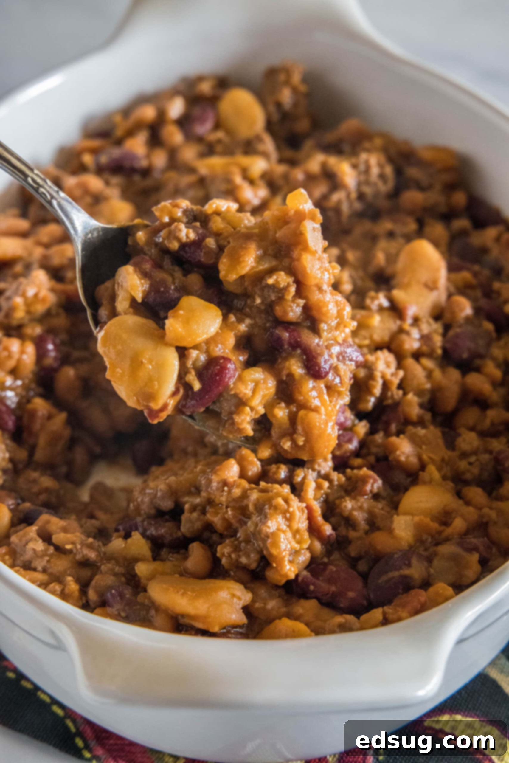 This hearty calico beans recipe is a sweet n' smoky side dish perfect for cookouts, potlucks, and holidays. Make it in the oven or crock pot! A spoon lifting calico beans from a casserole dish.