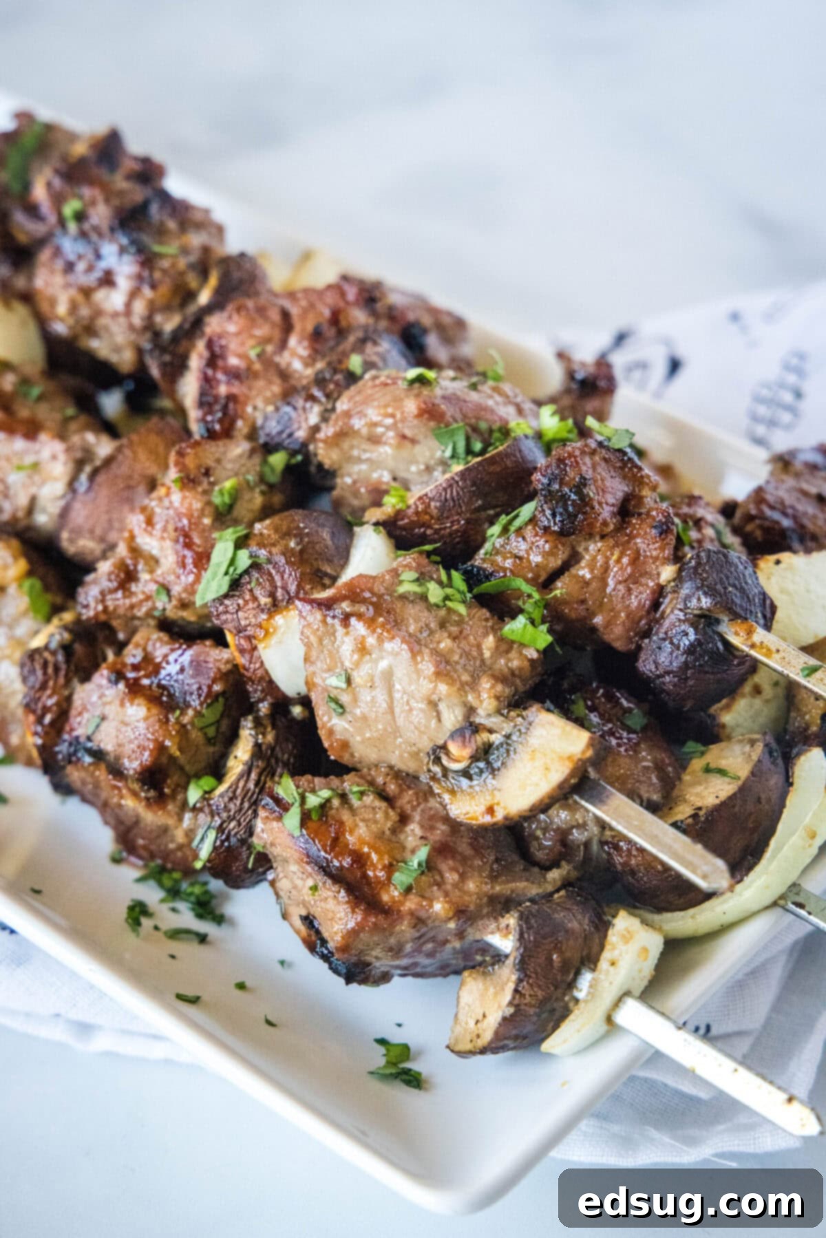 A stack of beef kabobs on a plate, garnished with green onions