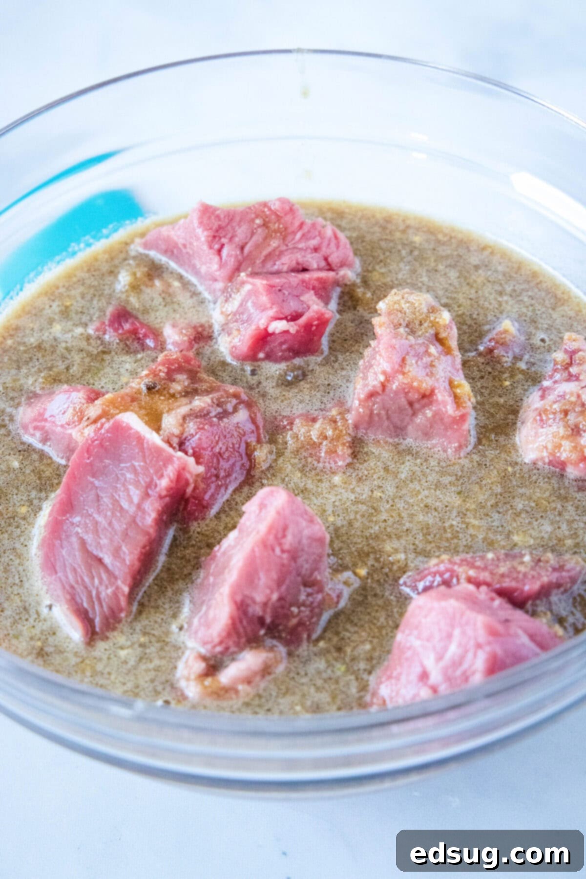 Cubes of beef in a mixing bowl with the ginger soy marinade, ready to tenderize