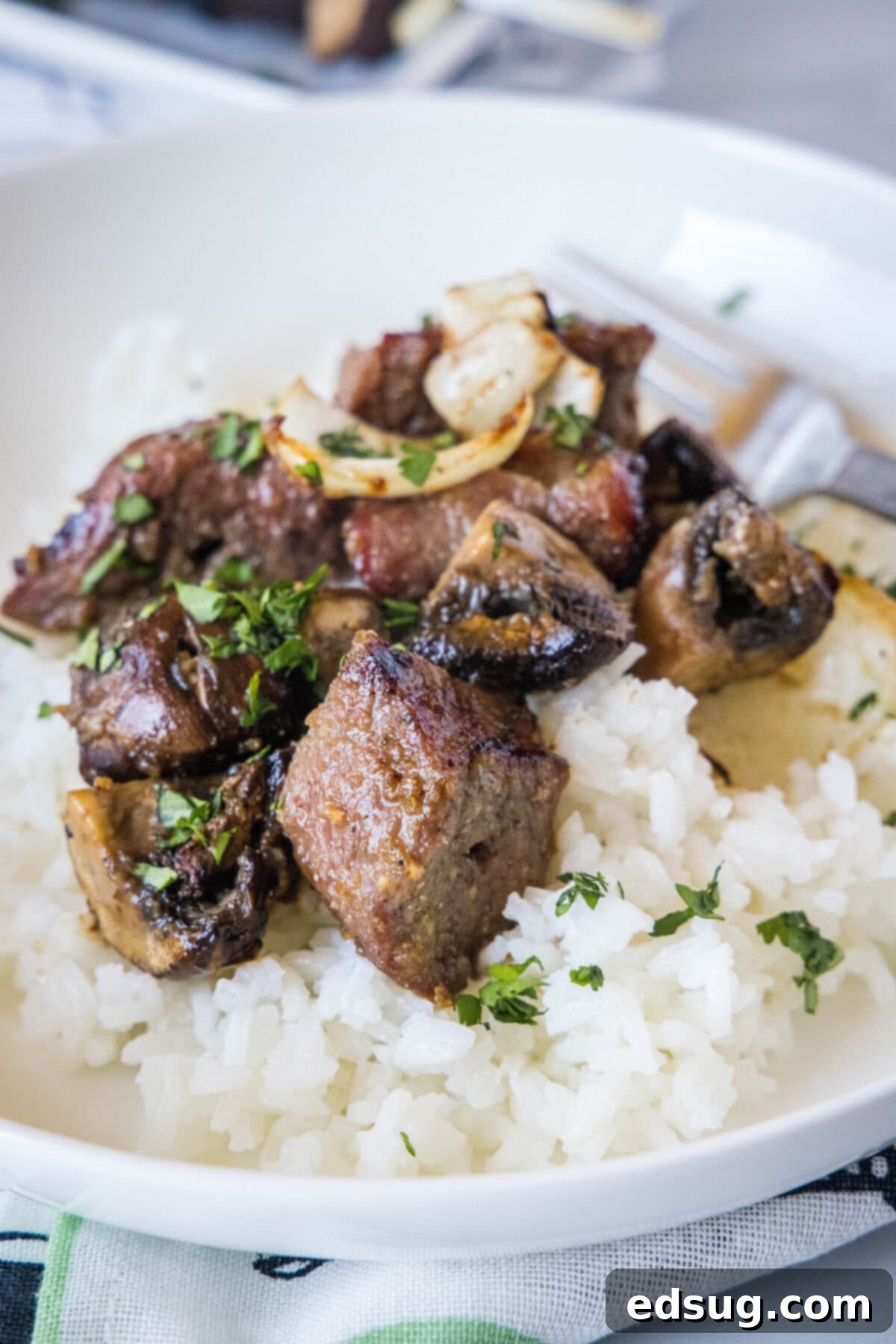 Close up of beef cubes on top of rice on a plate, garnished with sesame seeds