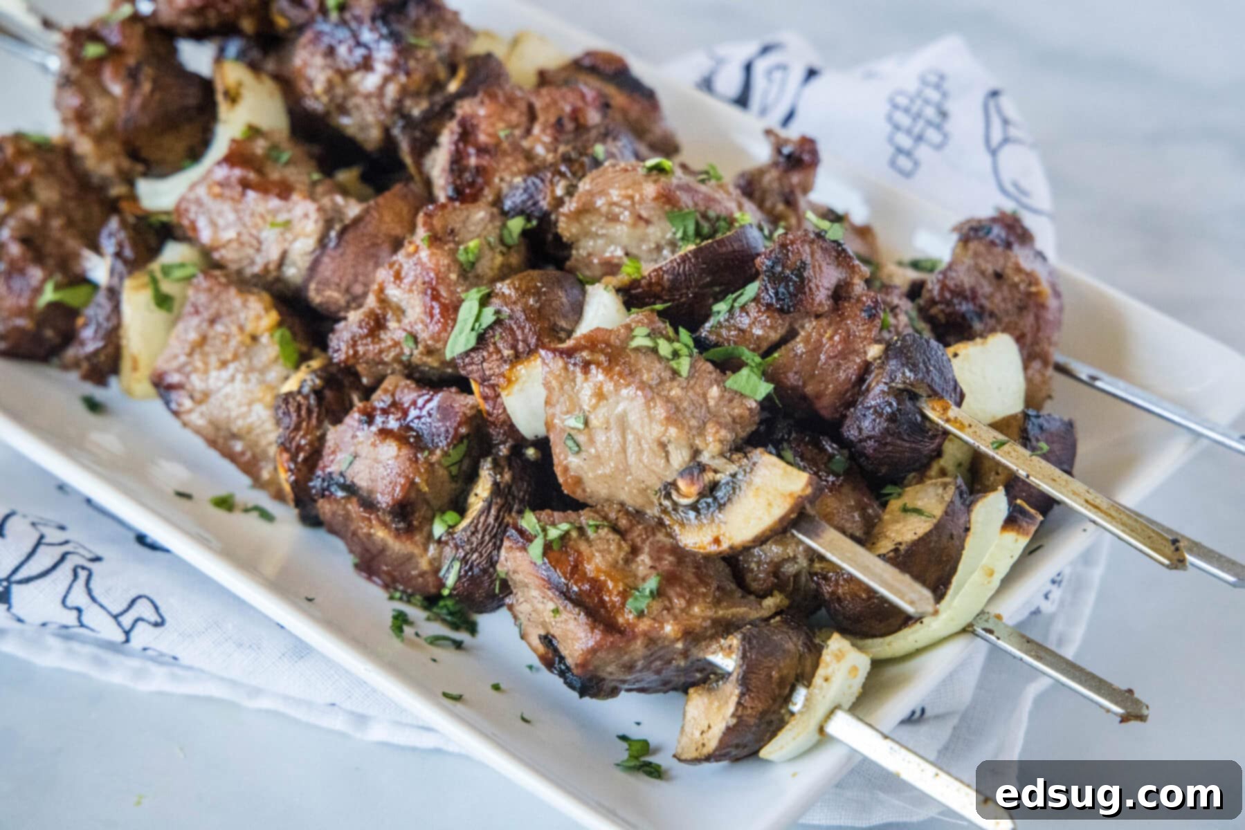 A stack of beef kabobs on a plate, garnished with fresh herbs