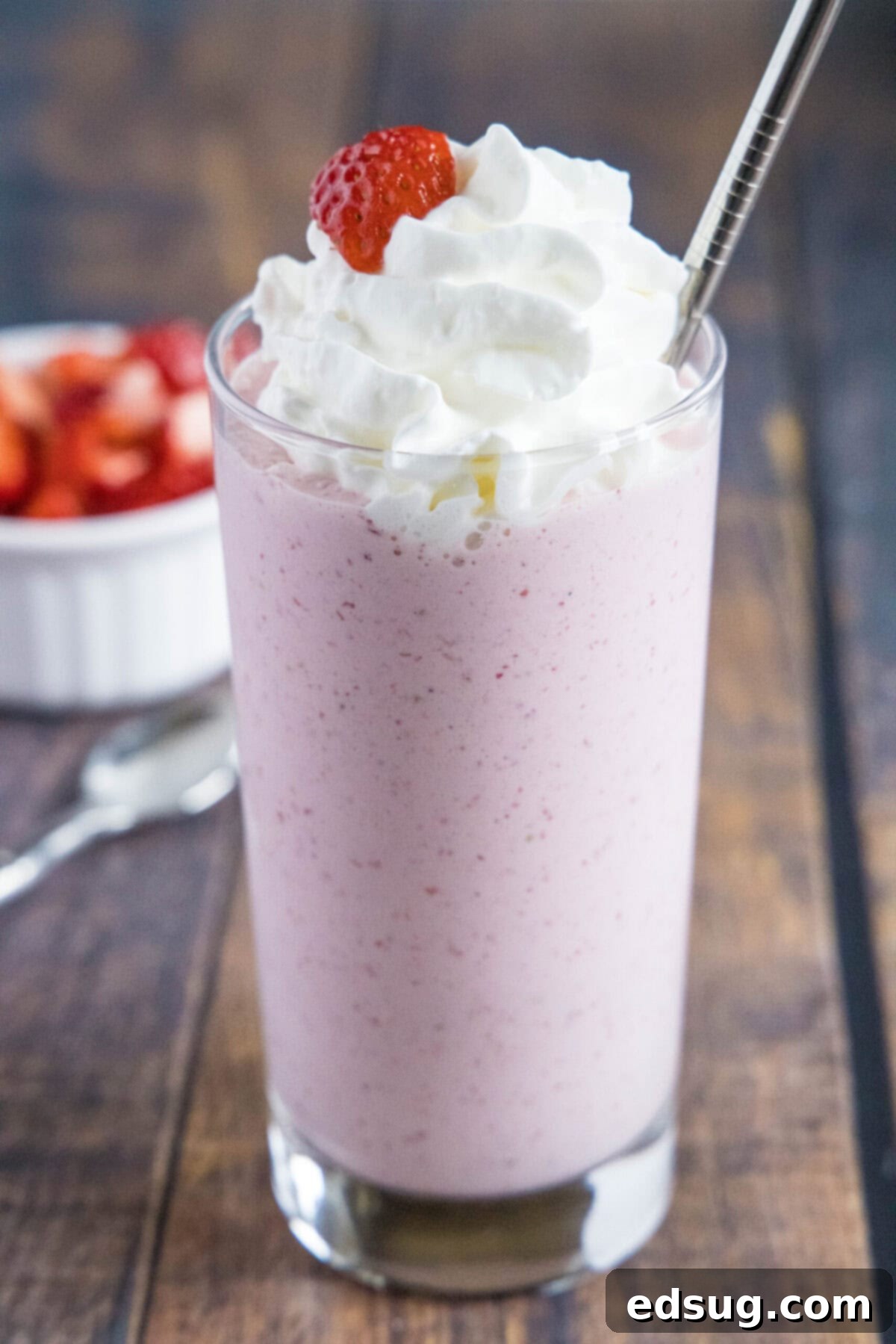 These 5-ingredient strawberry milkshakes are full of nostalgia and flavor. They're quick and easy to make, and absolutely delicious. Close up of a glass of strawberry milkshake with whipped cream, a strawberry garnish, and a straw