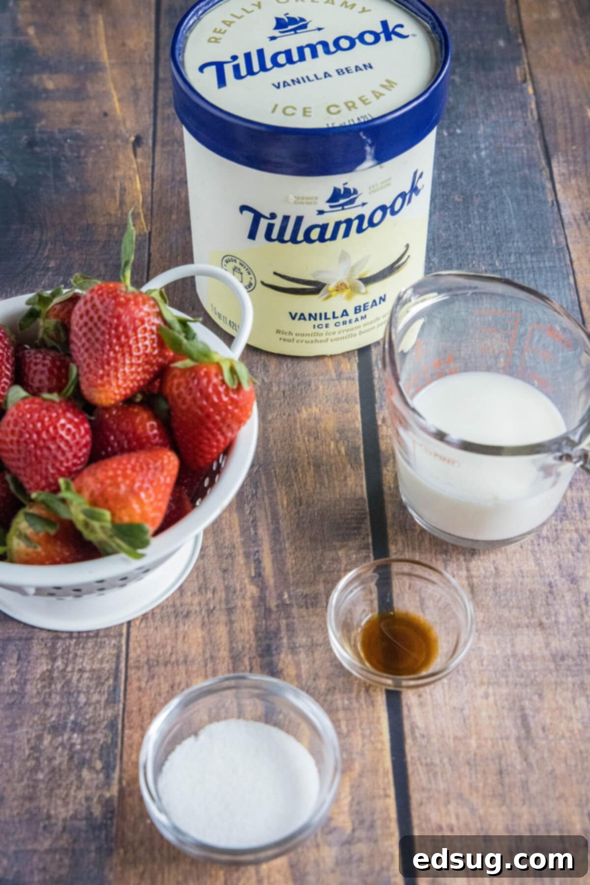 These 5-ingredient strawberry milkshakes are full of nostalgia and flavor. They're quick and easy to make, and absolutely delicious. A counter with a bowl of fresh strawberries, a carton of Tillamook vanilla ice cream, a bowl of sugar, a bowl of vanilla, and a pyrex of milk