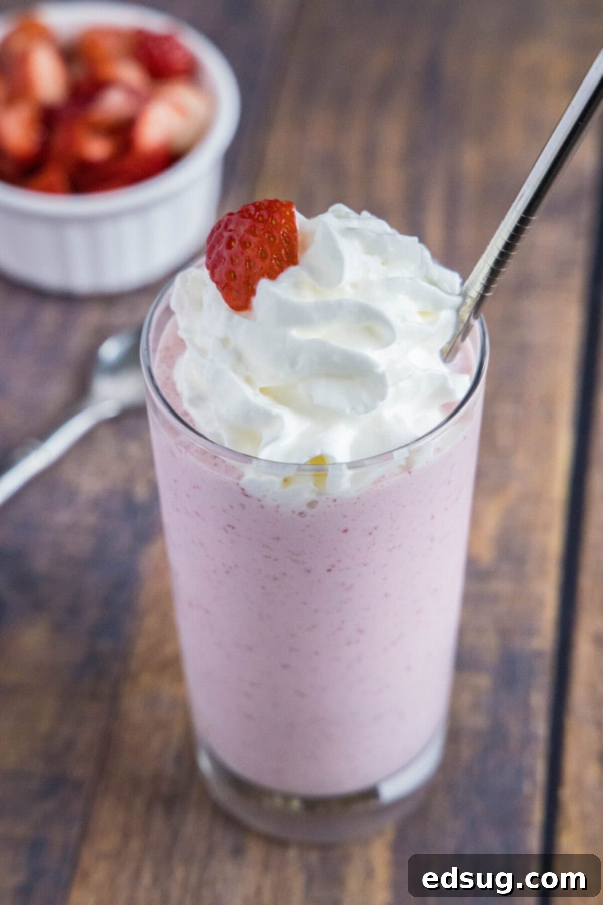 These 5-ingredient strawberry milkshakes are full of nostalgia and flavor. They're quick and easy to make, and absolutely delicious. Overhead view of a strawberry milkshake with whipped cream, with a bowl of strowberries in the background.