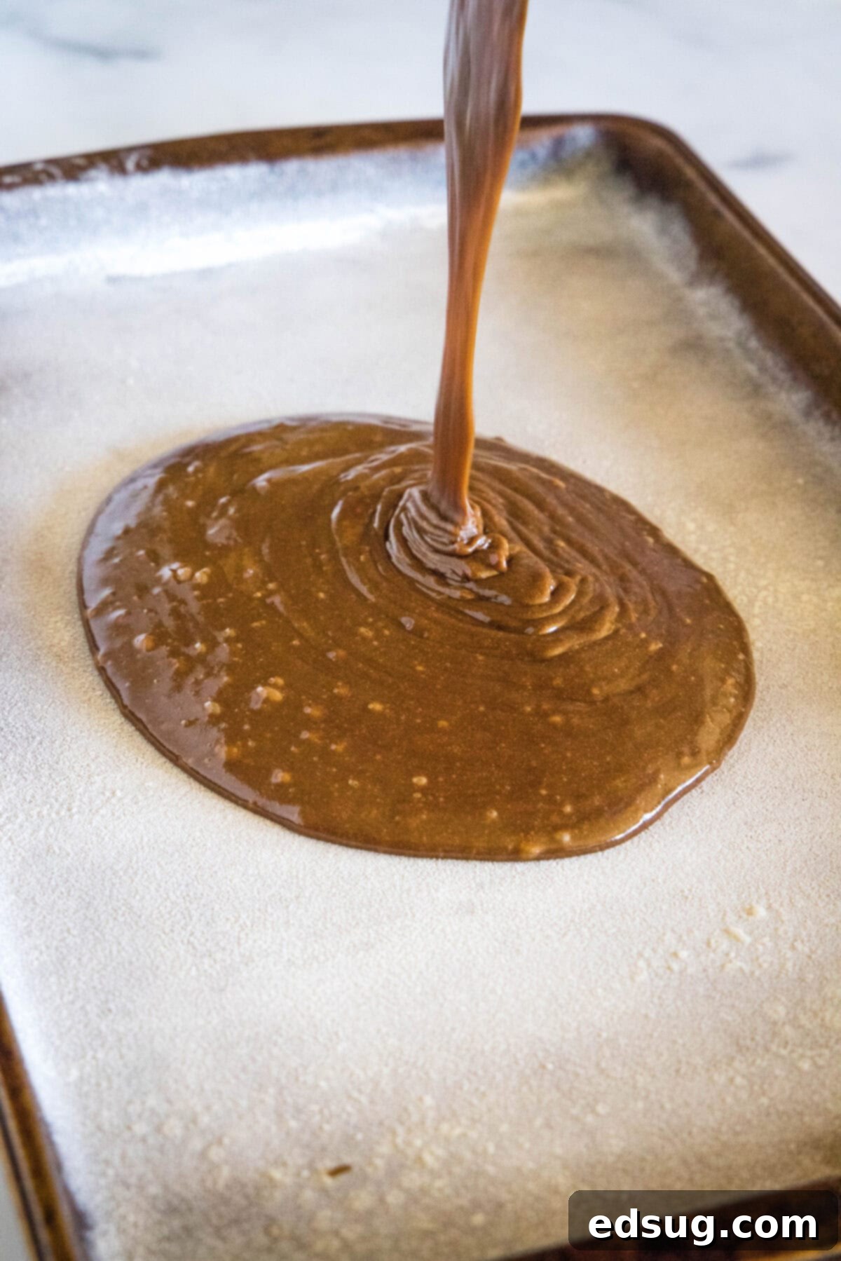 Irresistible Texas Sheet Cake 7 Smooth chocolate cake batter being poured into a greased and floured sheet pan for baking.