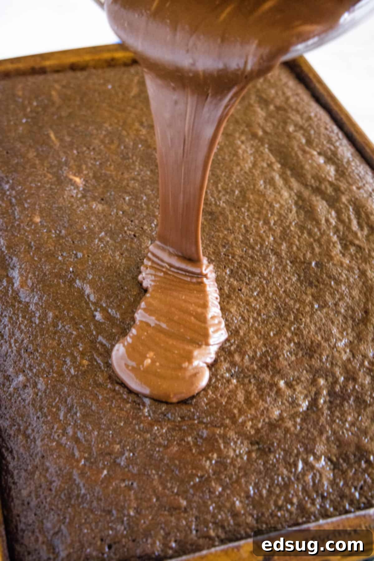 Irresistible Texas Sheet Cake 10 Warm chocolate frosting being poured and spread over a freshly baked Texas Sheet Cake.
