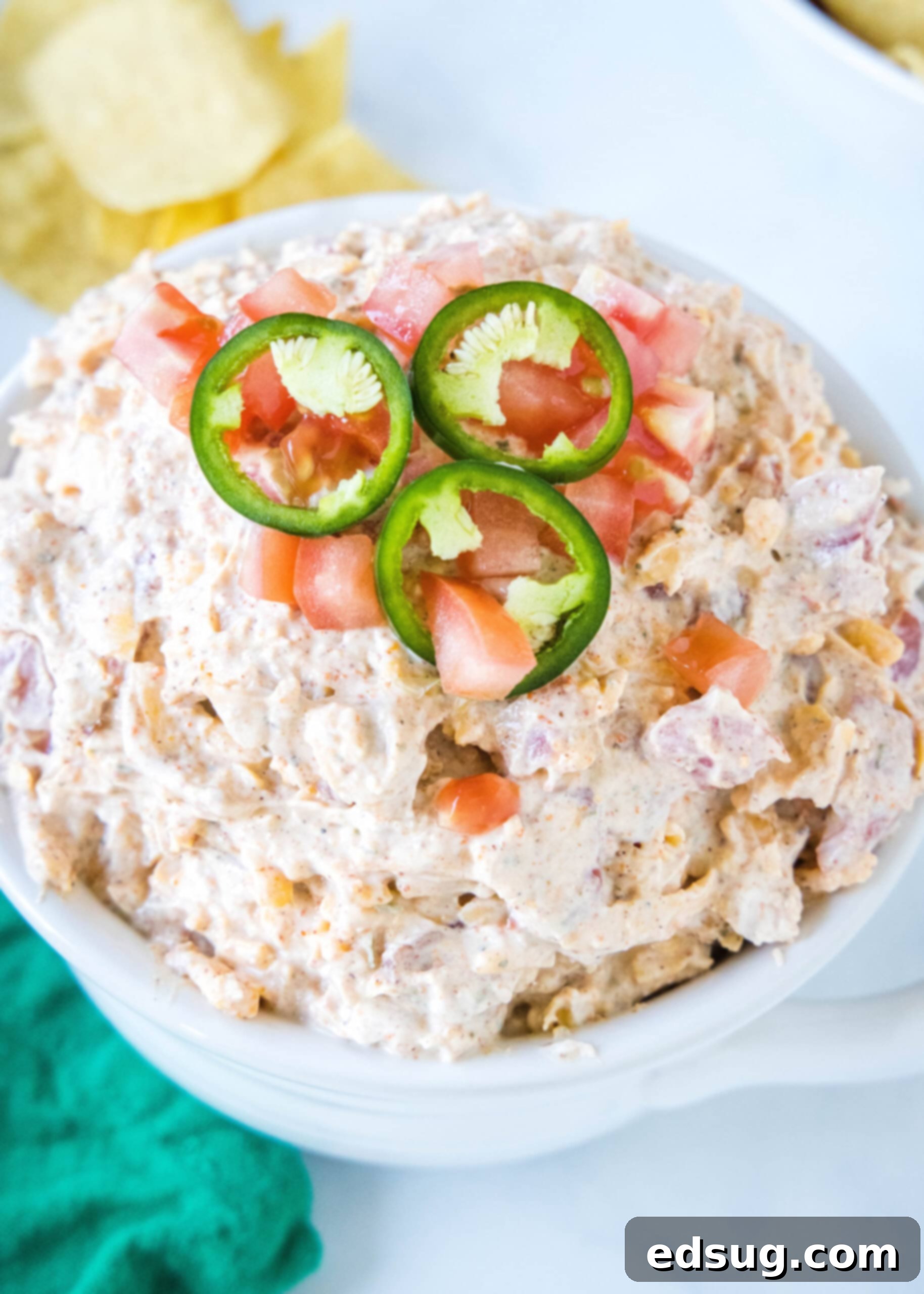 Boat dip is a cool, creamy taco dip inspired by the viral TikTok recipe! It's the perfect easy appetizer for your next summer BBQ or potluck. Close-up of boat dip topped with sliced jalapeños in a white bowl, with a serving spoon.