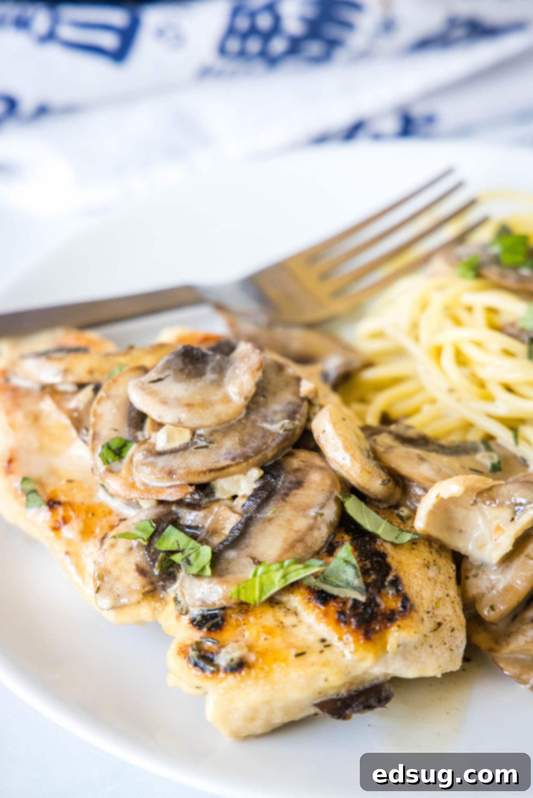 Chicken Marsala served with spaghetti on a plate next to a fork, topped with mushrooms and a rich, creamy Marsala wine sauce.
