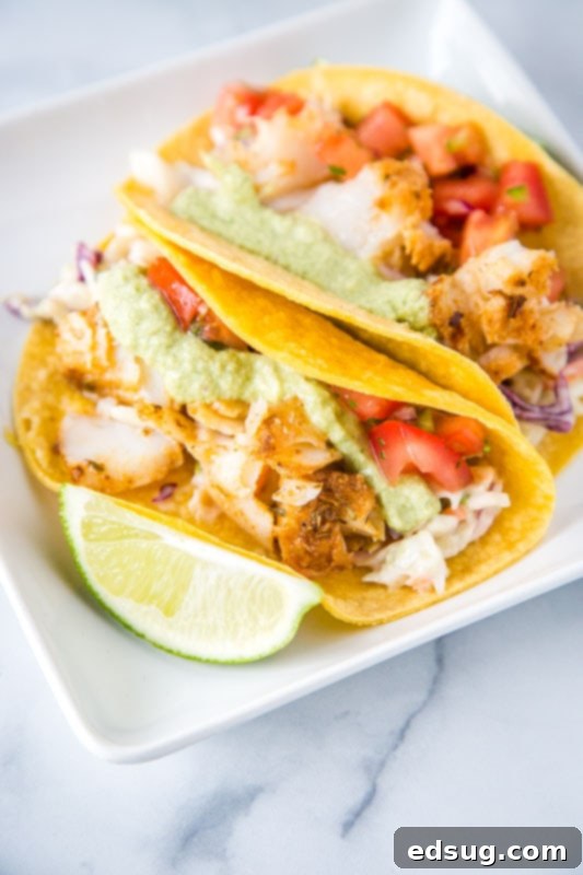Zesty Fish Tacos 3 Close-up of flaky cod fish tacos with creamy poblano sauce, fresh pico de gallo, and a wedge of lime