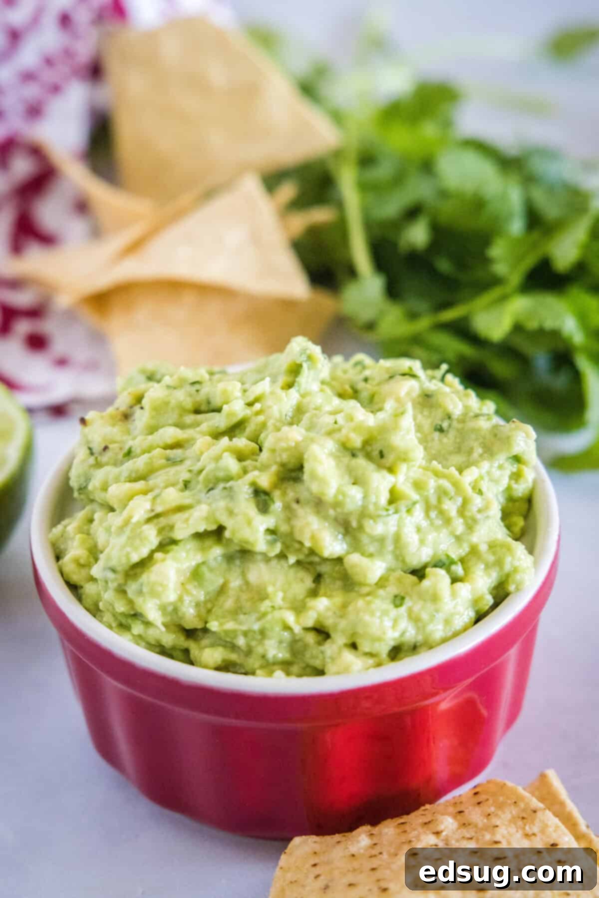 Smoky Garlic Guac Perfection 7 A beautifully presented serving bowl of roasted garlic guacamole, garnished with vibrant fresh cilantro and a lime wedge, resting on a rustic wooden board, accompanied by a small pile of crispy tortilla chips.