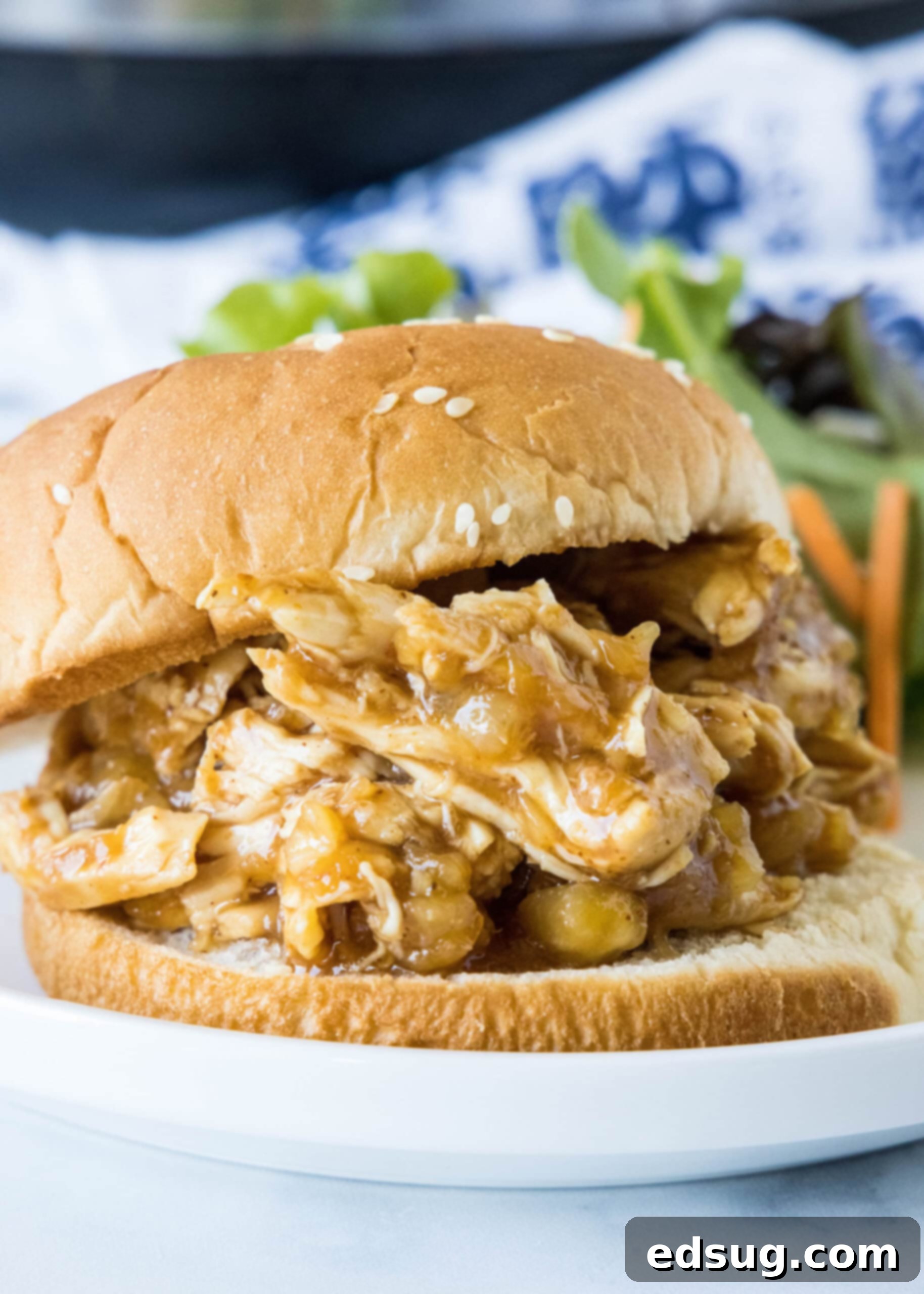 A delectable slow cooker Hawaiian chicken sandwich, garnished with fresh toppings, sits on a plate next to a vibrant green salad.