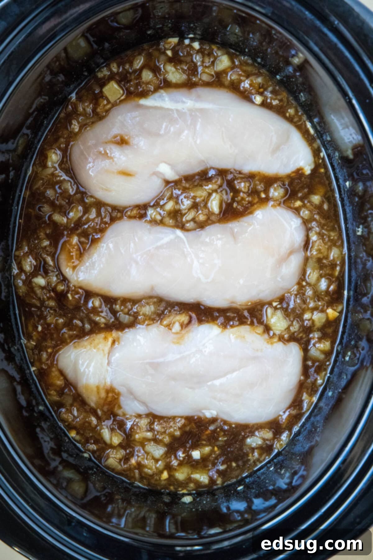 Three plump chicken breasts neatly nestled into the flavorful Hawaiian cooking sauce, ready for slow cooking.